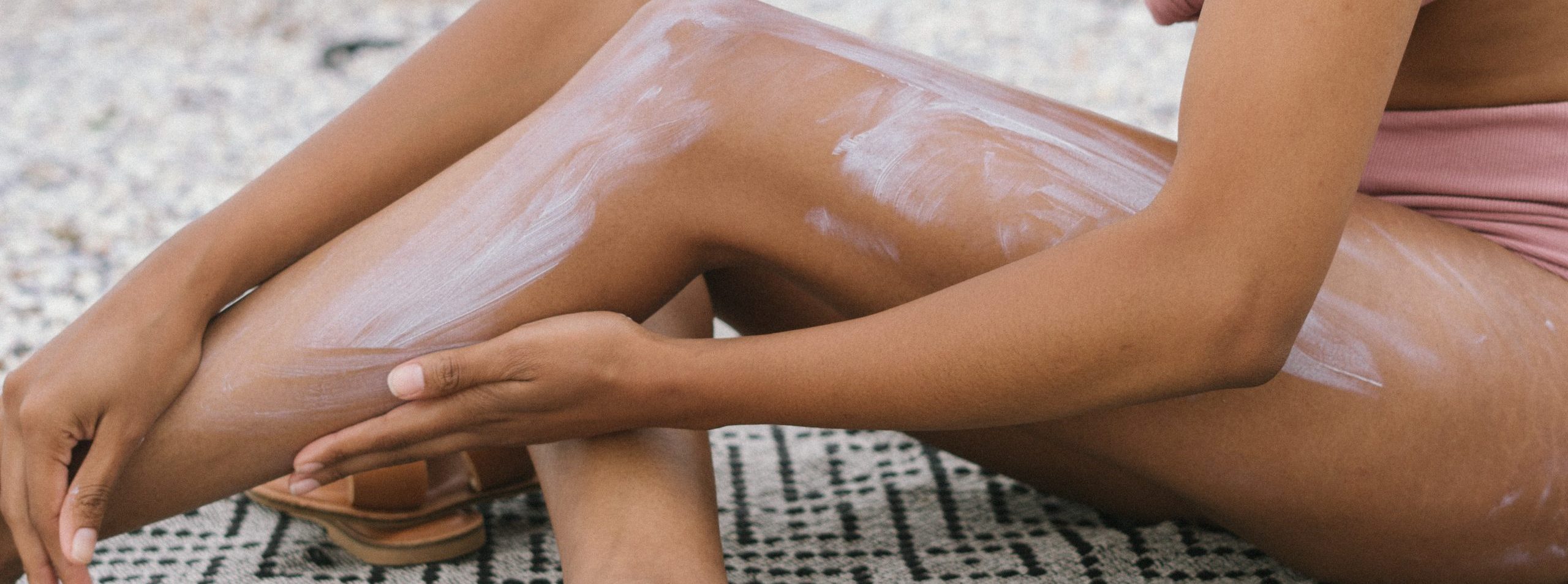 A woman applies sun cream to her body.