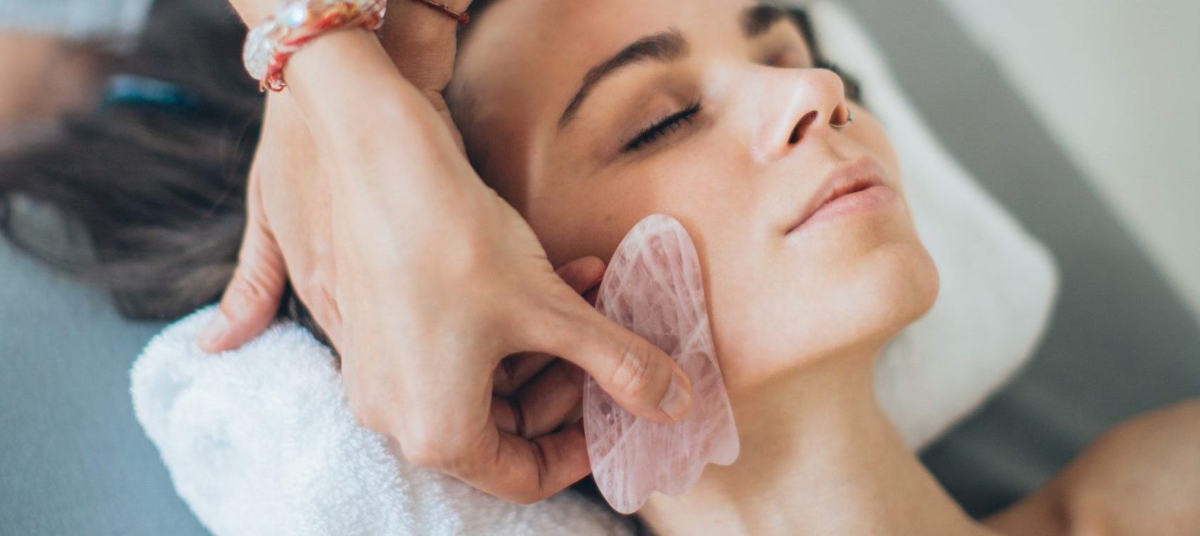 A practitioner massages the face of a woman with a Gua sha tool to improve her circulation.