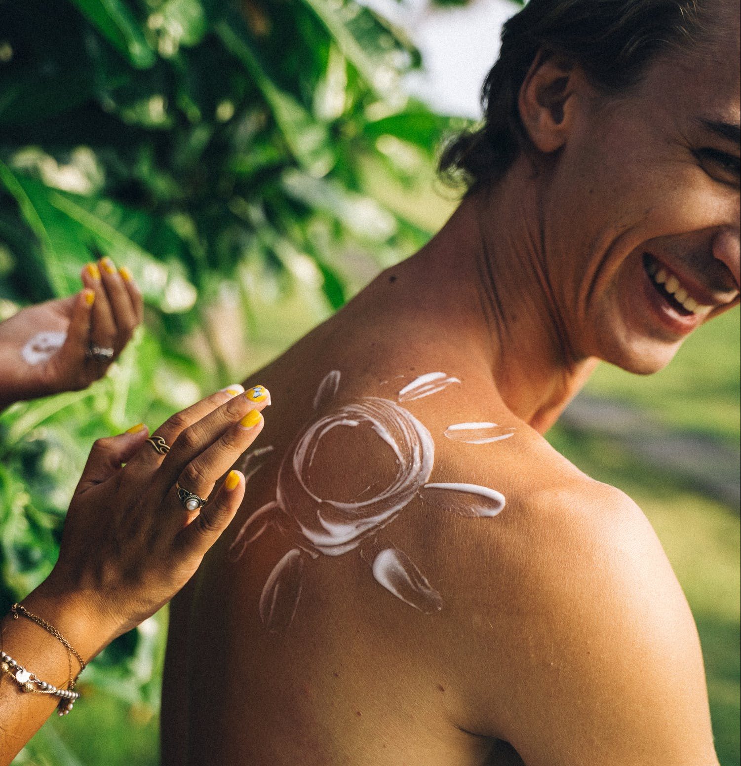 A young man enjoying having sun cream applied to his back.