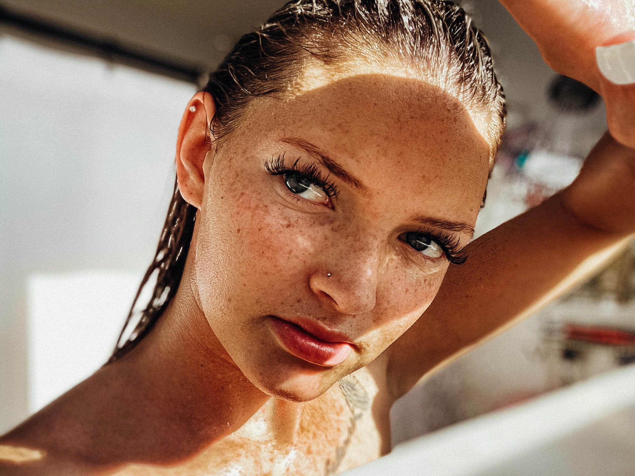 A woman with freckles shields her face from the sun with her hand.