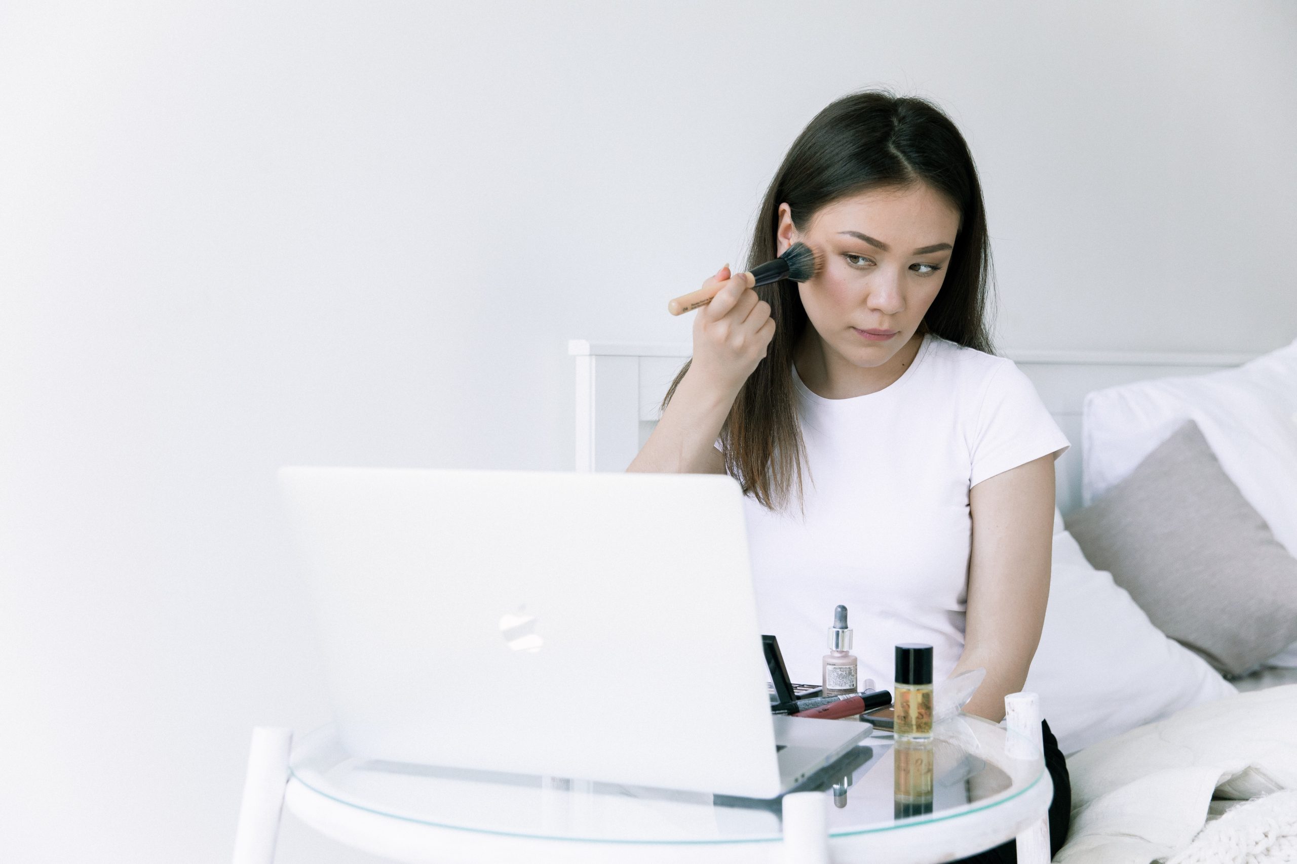 A woman applies makeup to achieve glass skin.