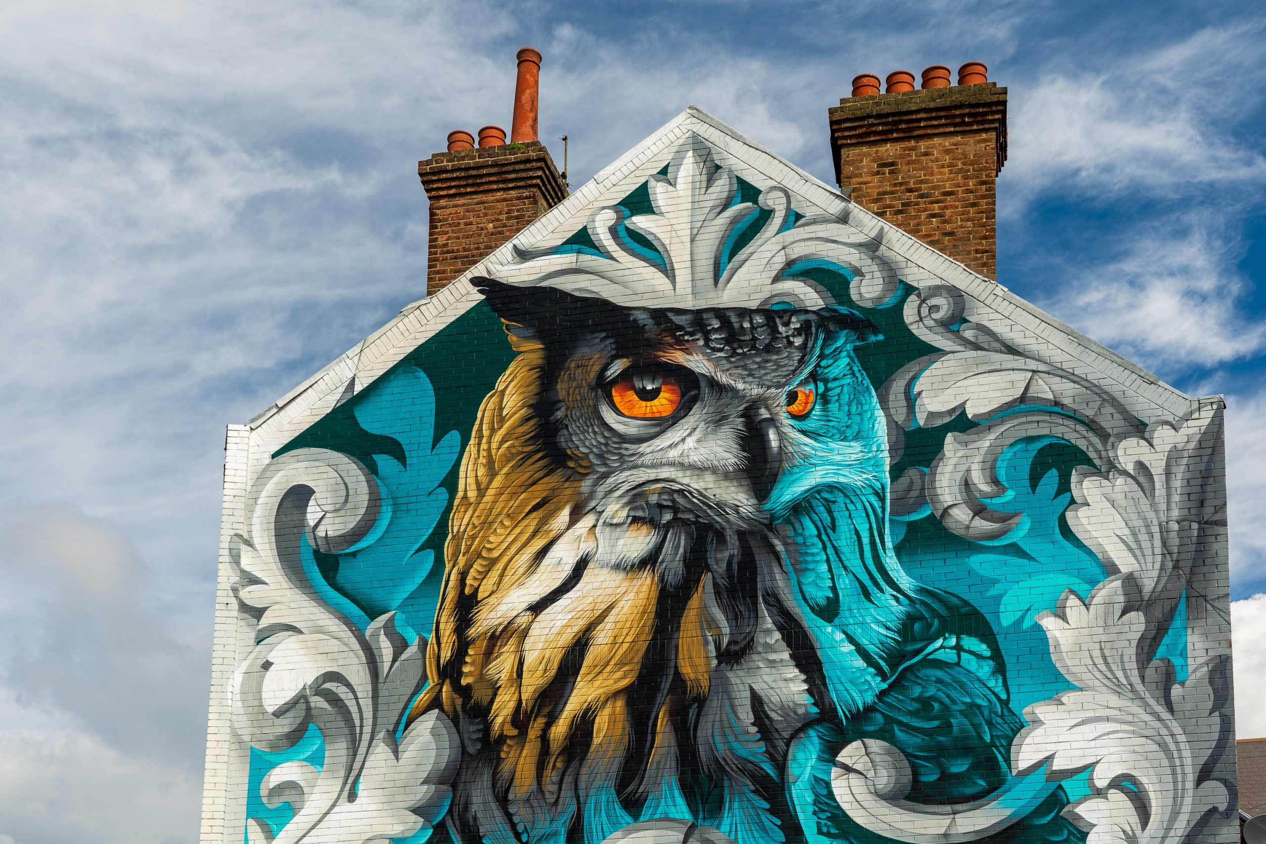 A mural of an owl with orange eyes painted on to the side of a building