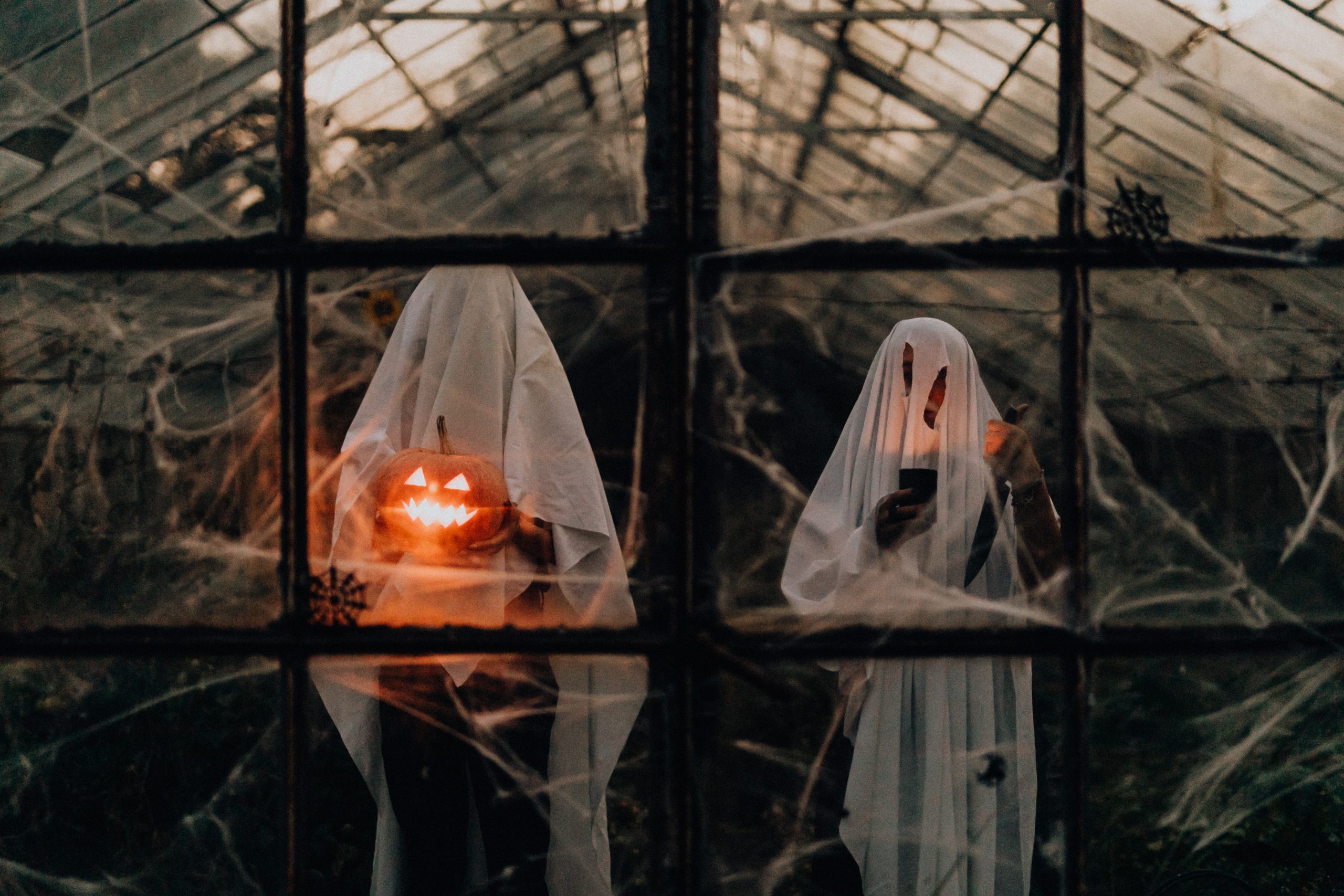 Two trick or treaters in ghost costumes holding a glowing pumpkin