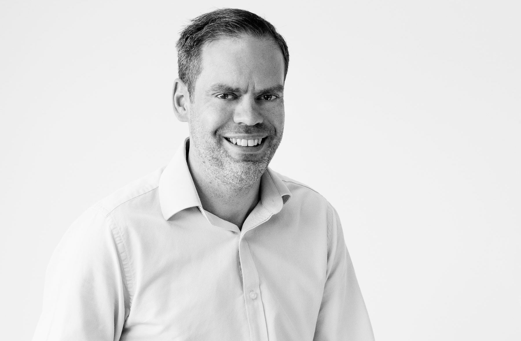 A black and white portrait of John Adams, the man behind DadBlogUK, smiling to camera