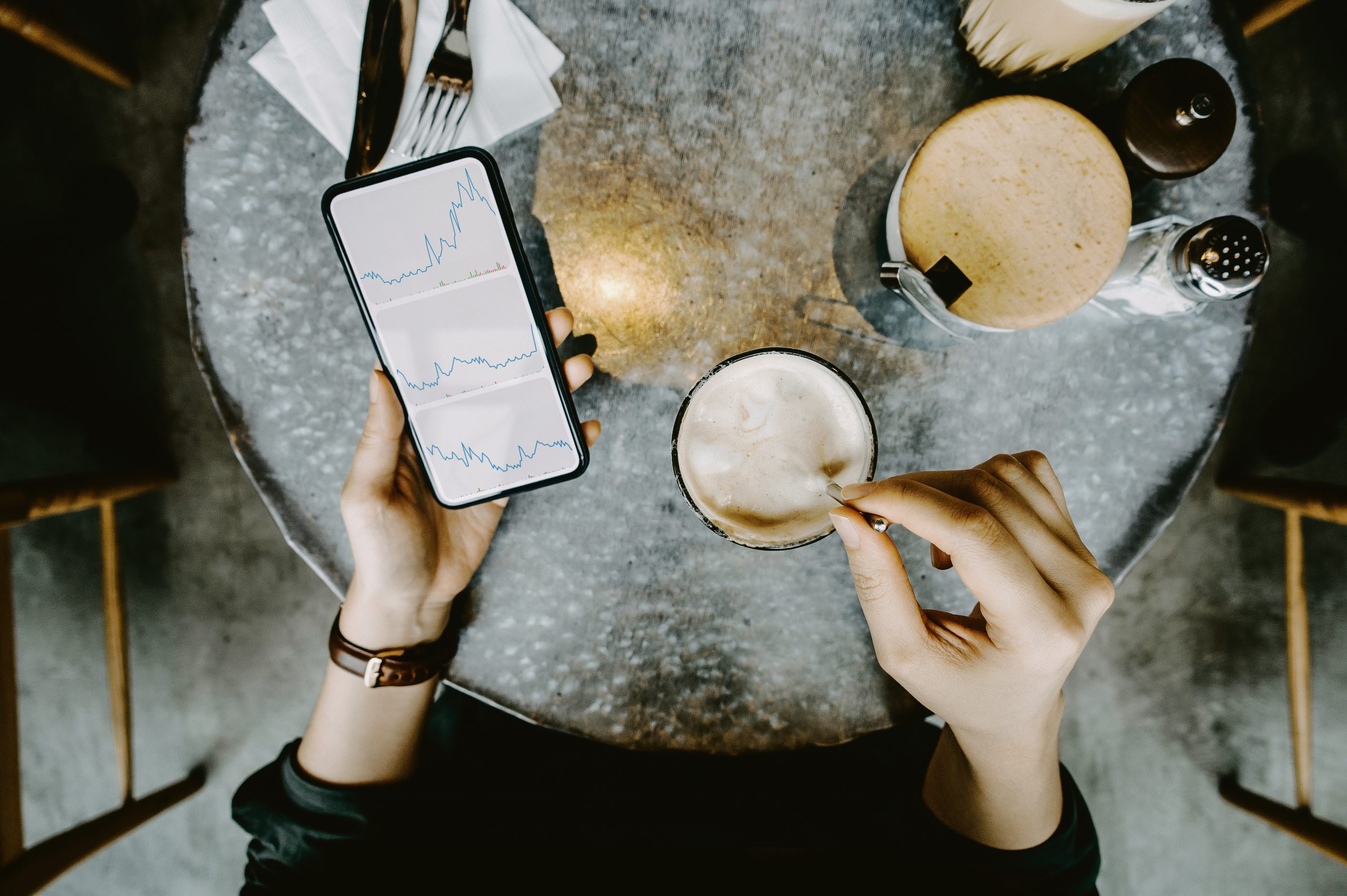 Overhead view of a woman checking her investments on a smartphone during a coffee break