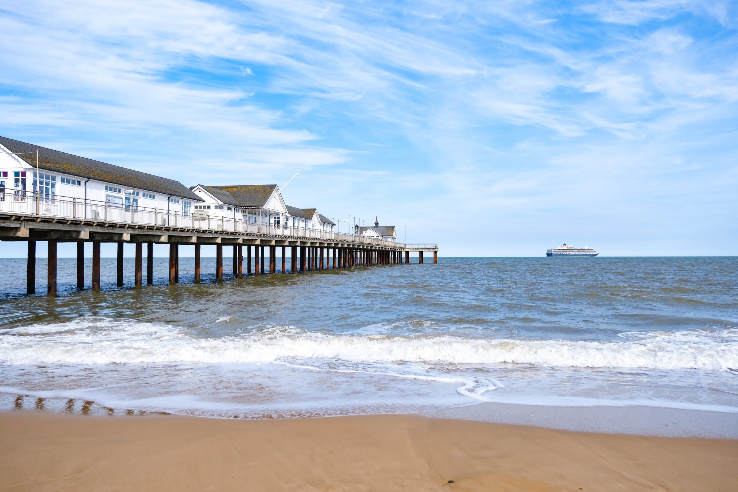 The pier of Southwold, Suffolk, on a sunny day with a ship sailing by on the horizon