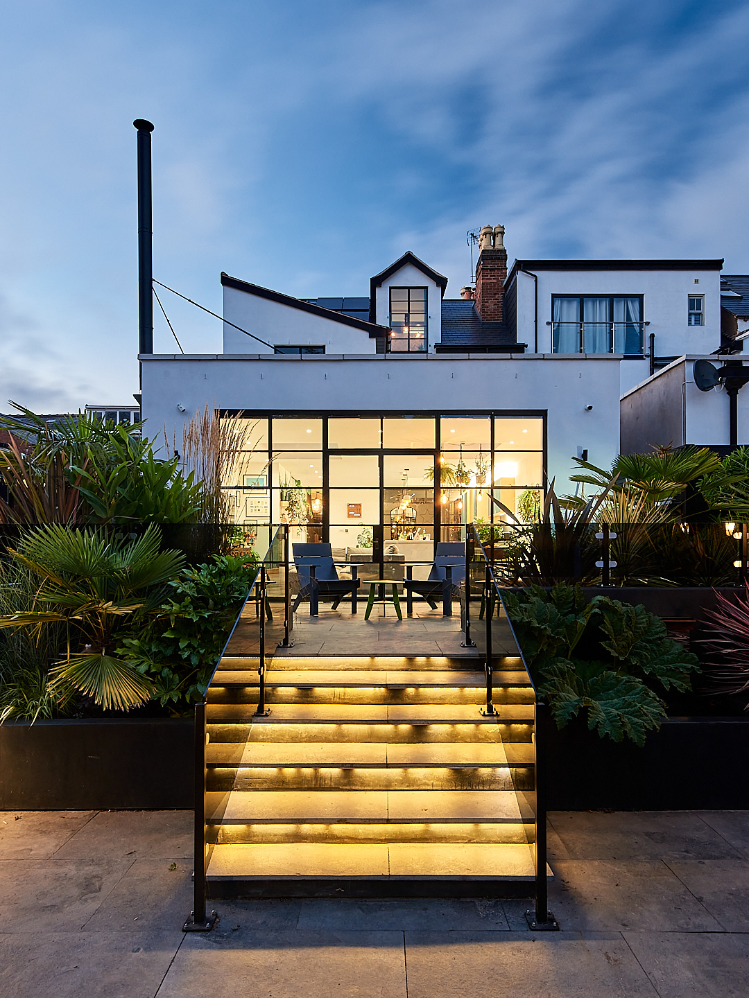 From the back porch, the Crittall windows of a renovated home reveal a cosy living room inside.