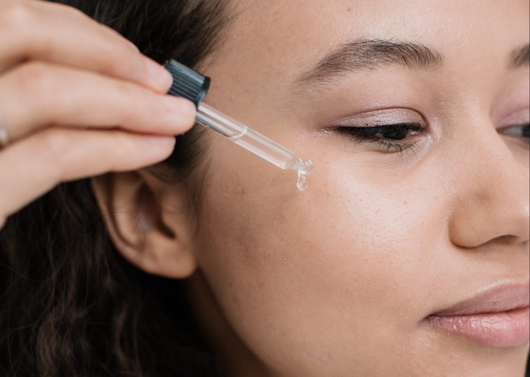 A woman applies skincare to her face with an eyedropper.