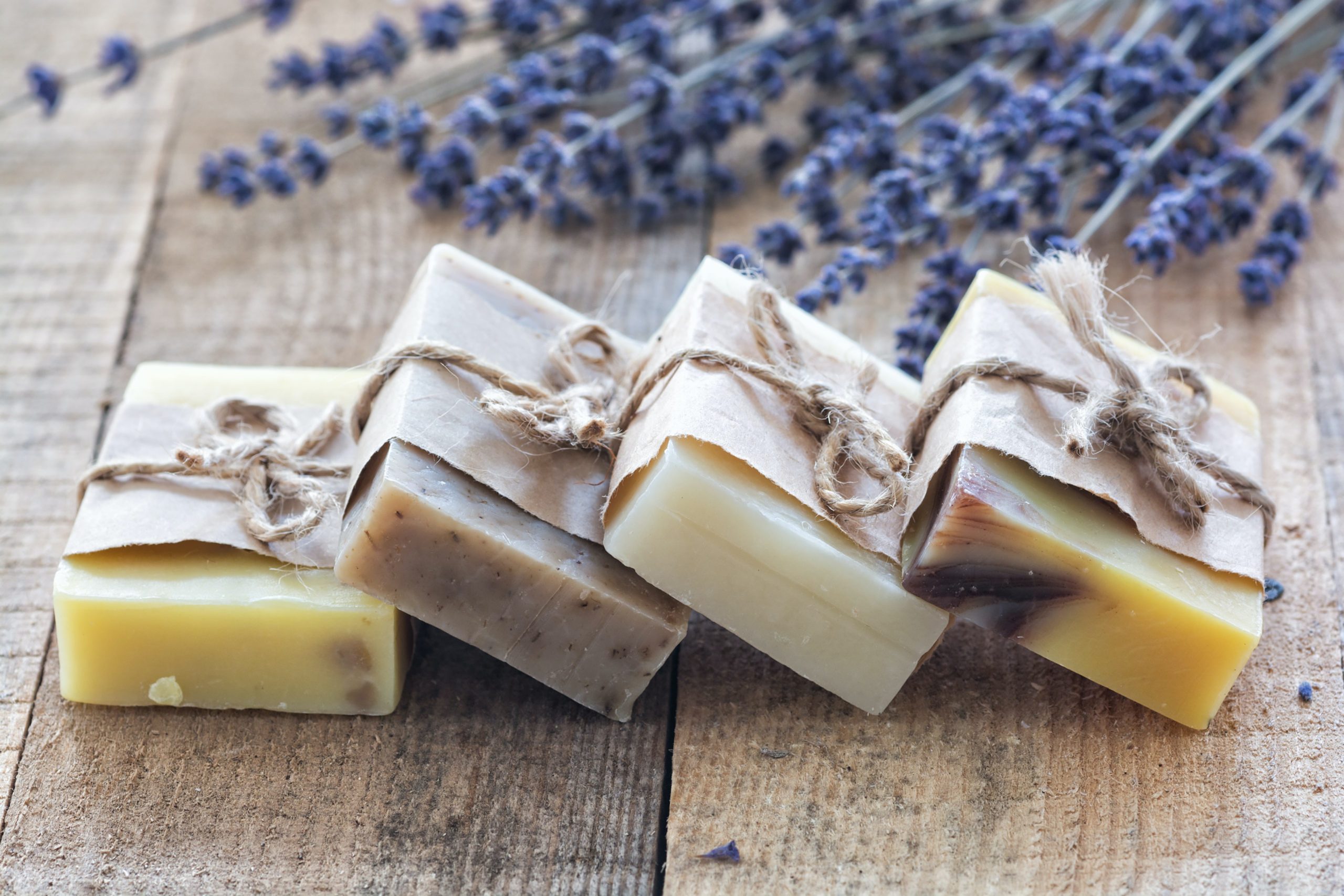 Four gift-wrapped homemade soaps on a table with flowers.