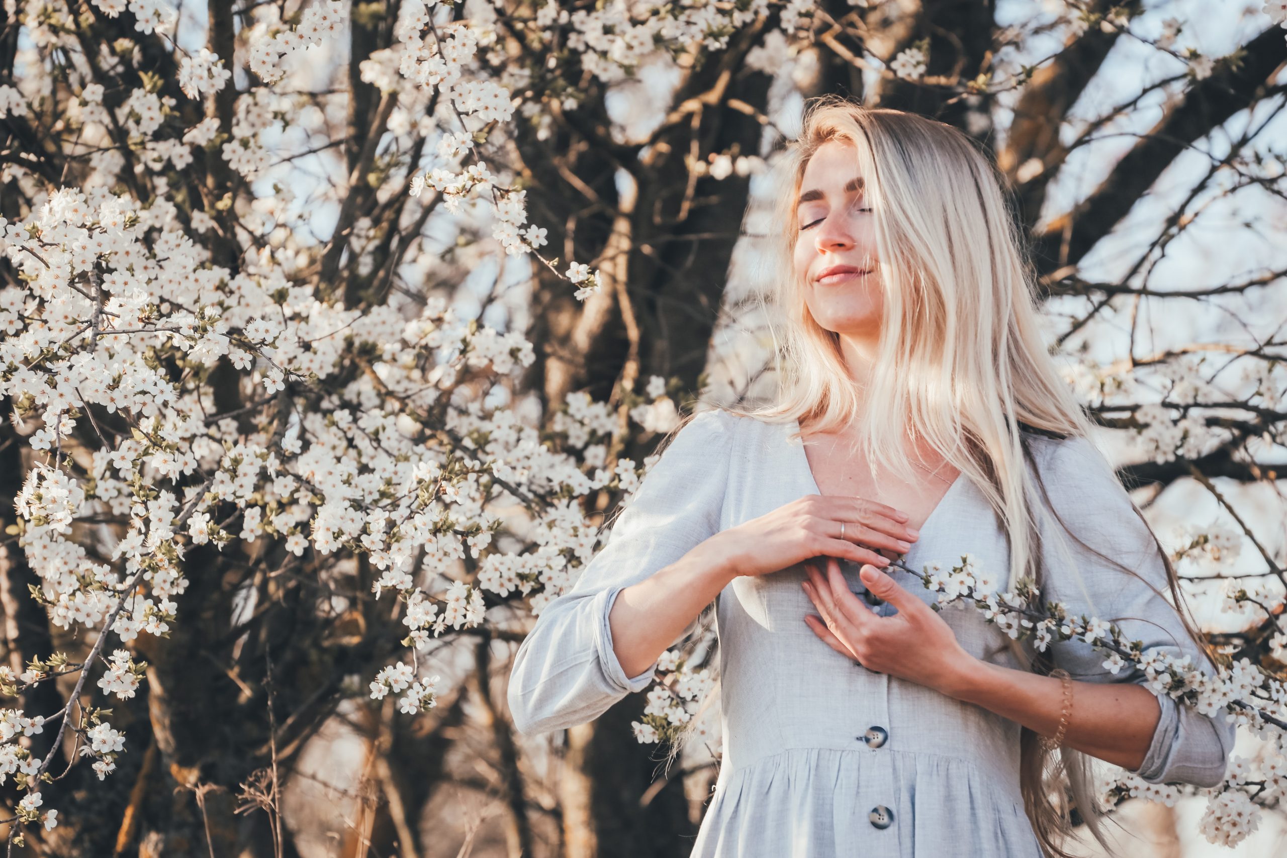 A young woman breathes mindfully in the park where trees are blossoming.