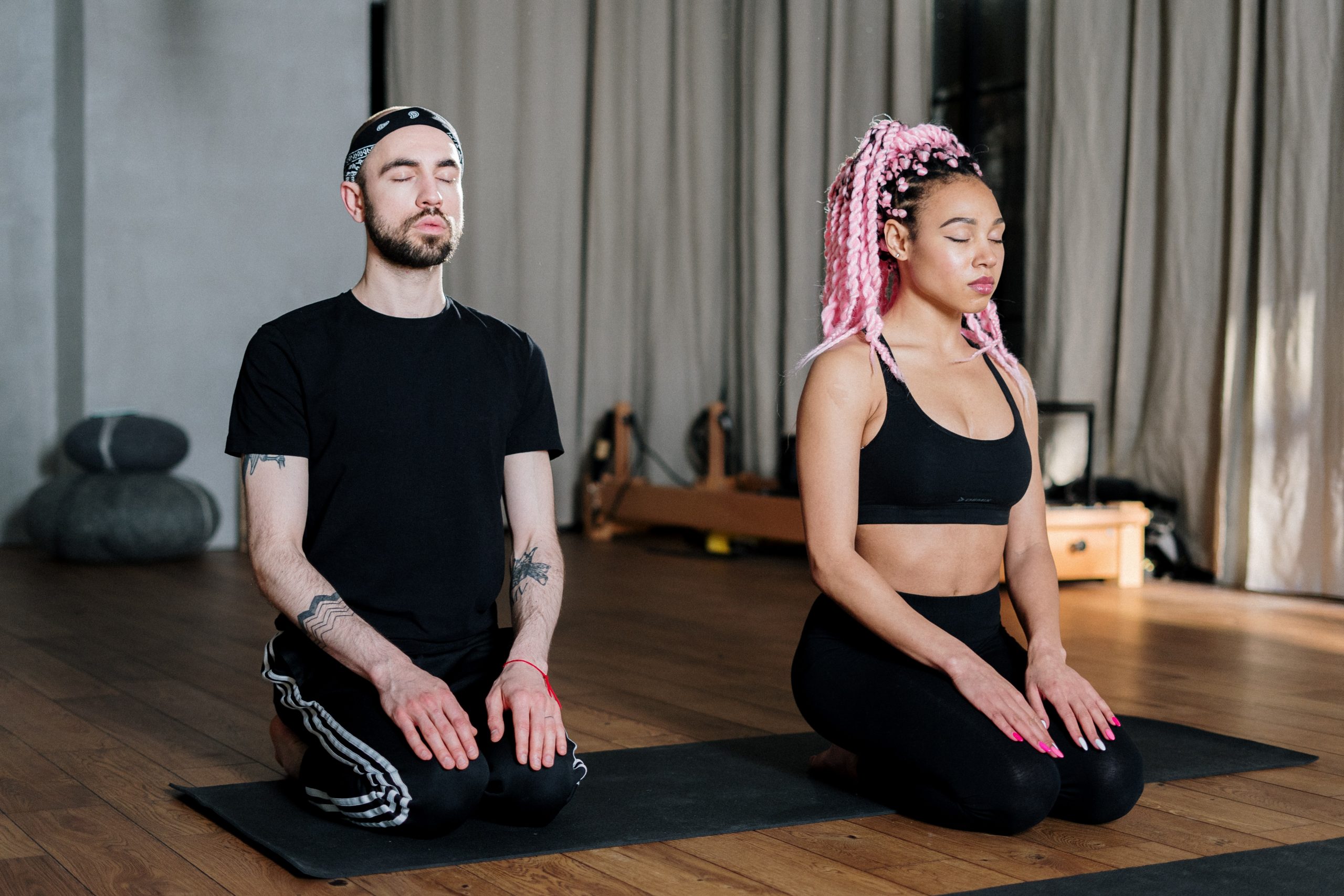 A white man and a black woman kneeling on a yoga mat practise mindful breathing.