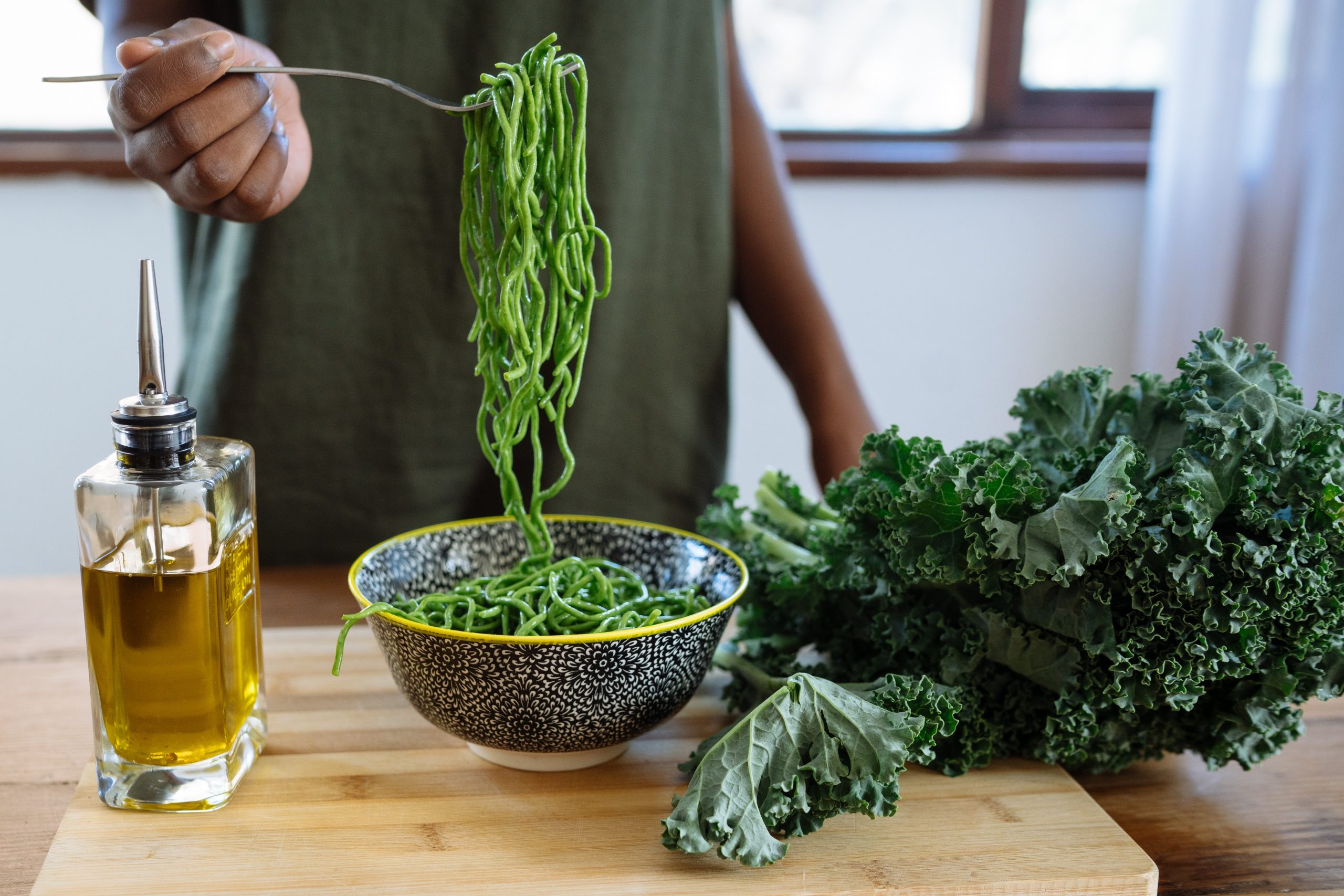 A woman in green tucks into a bowl of green noodles to improve her gut health.