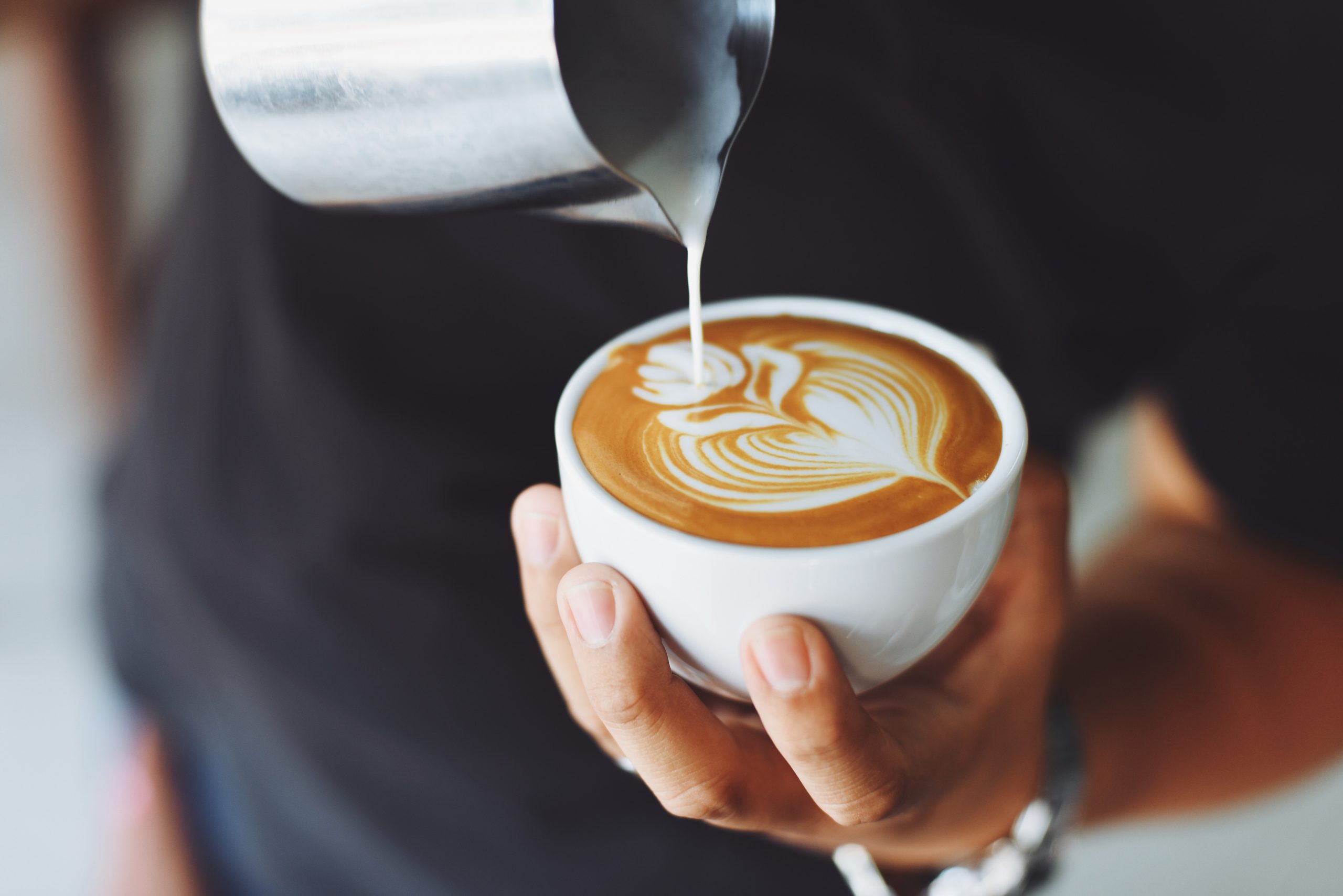 A barista pours a perfect cappuccino made with potato milk.