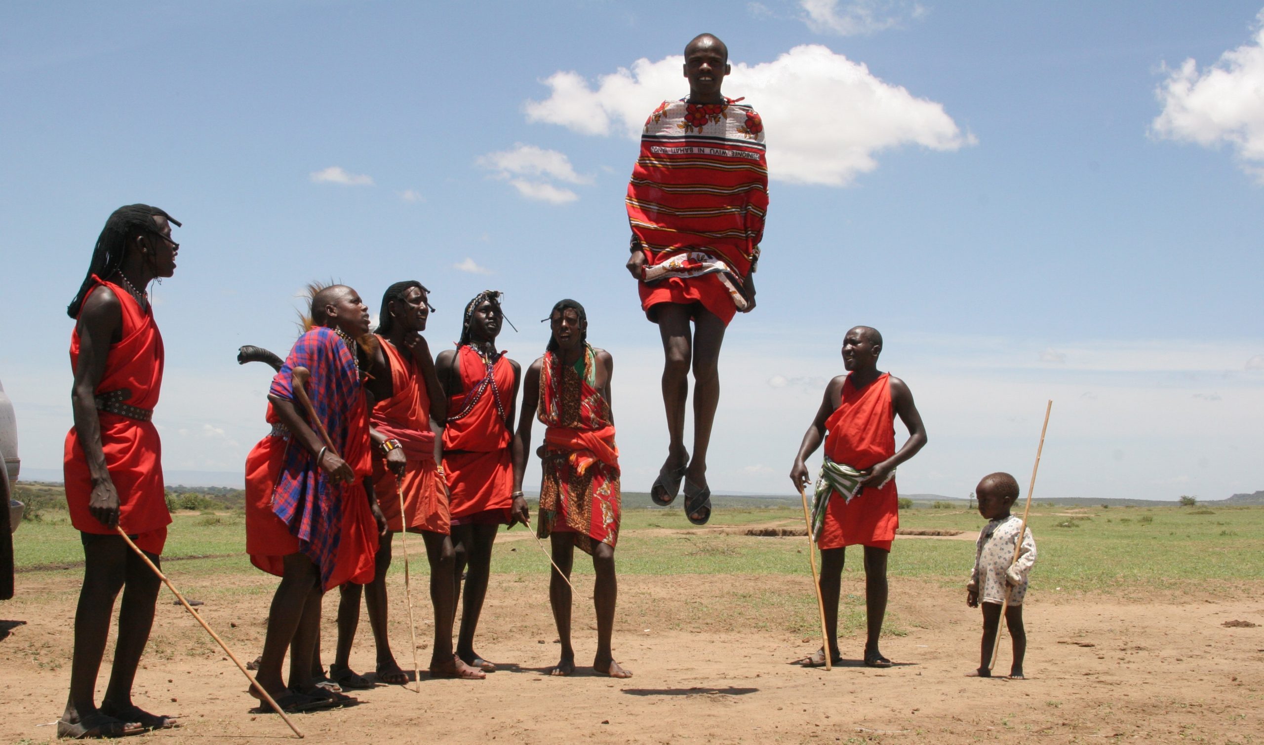 In red ceremonial garments, an African tribal group look on as one of them leaps into the air.