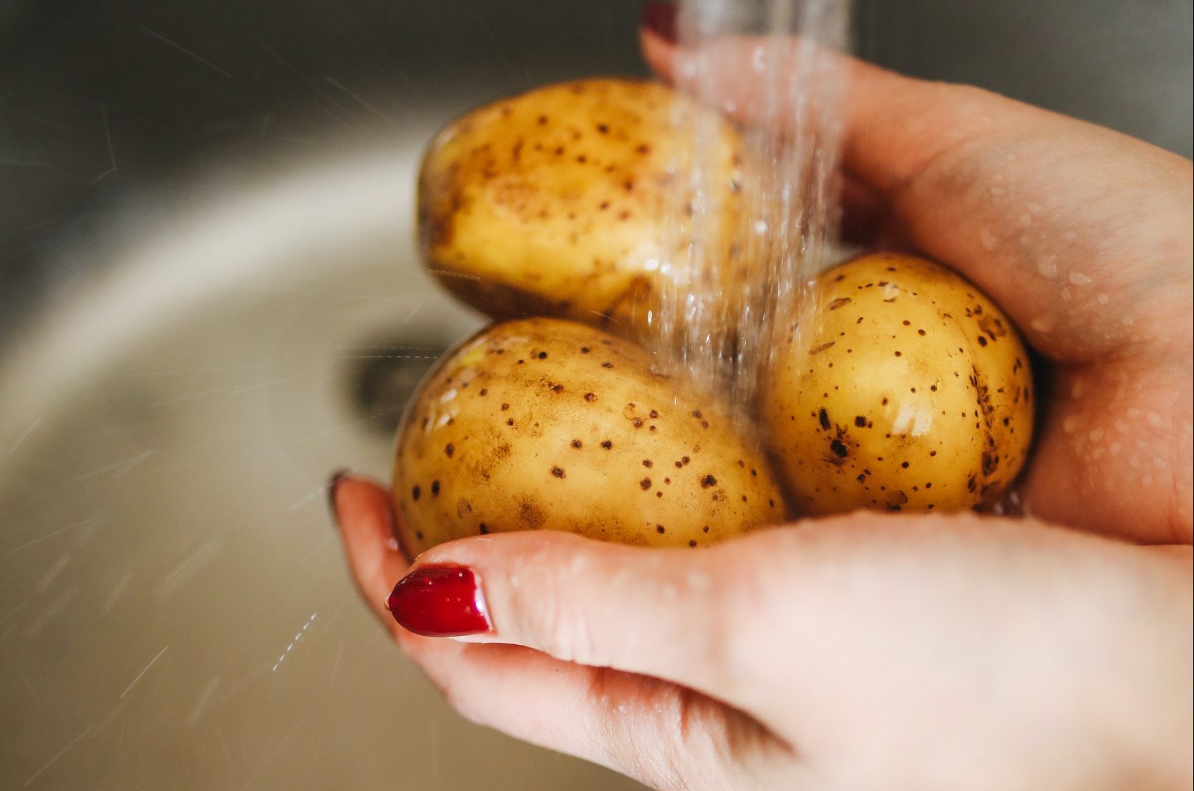 A woman's hands washing potatoes under running water.