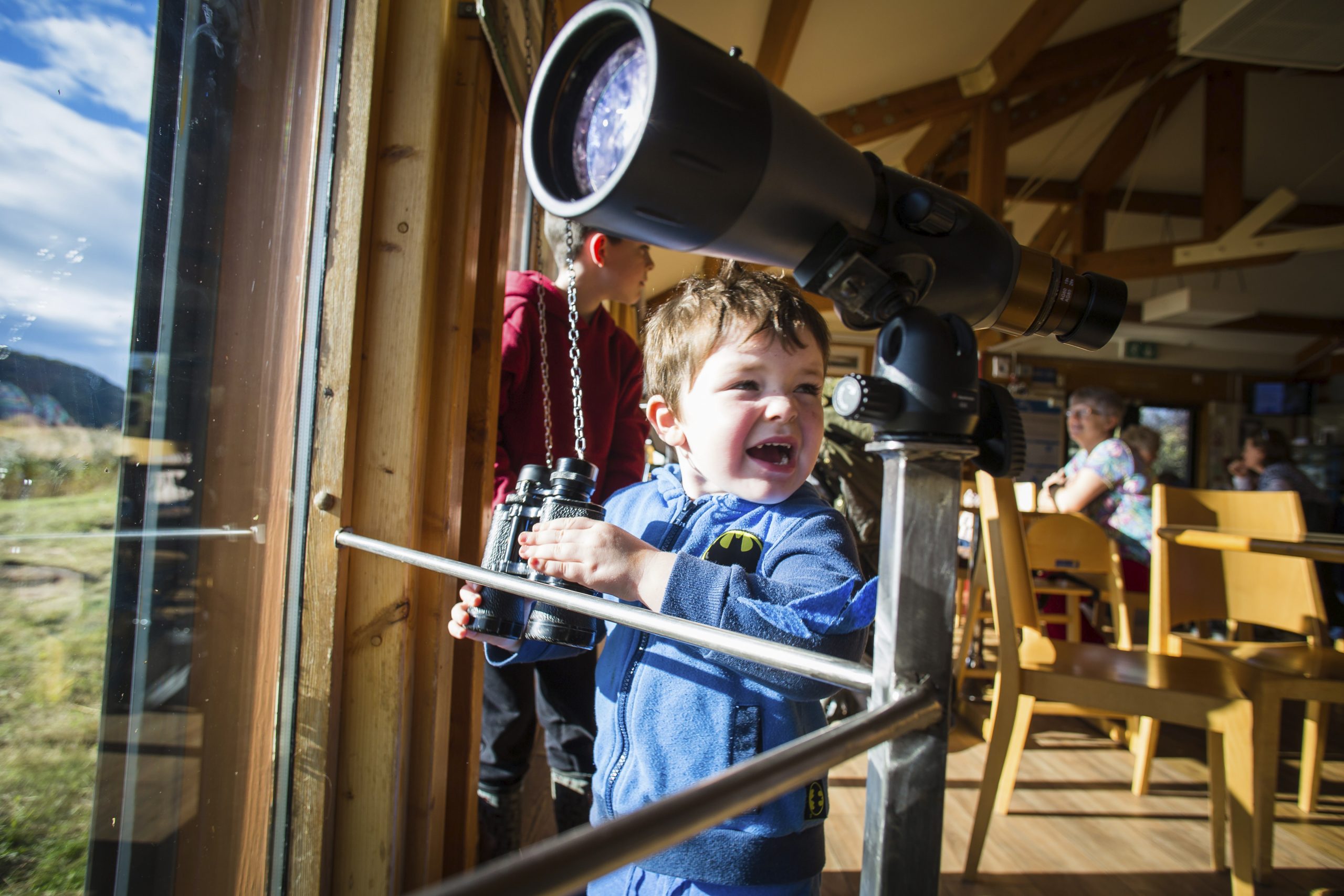 A young boy birdwatches with binoculars at Conwy RSPB Reserve, North Wales.