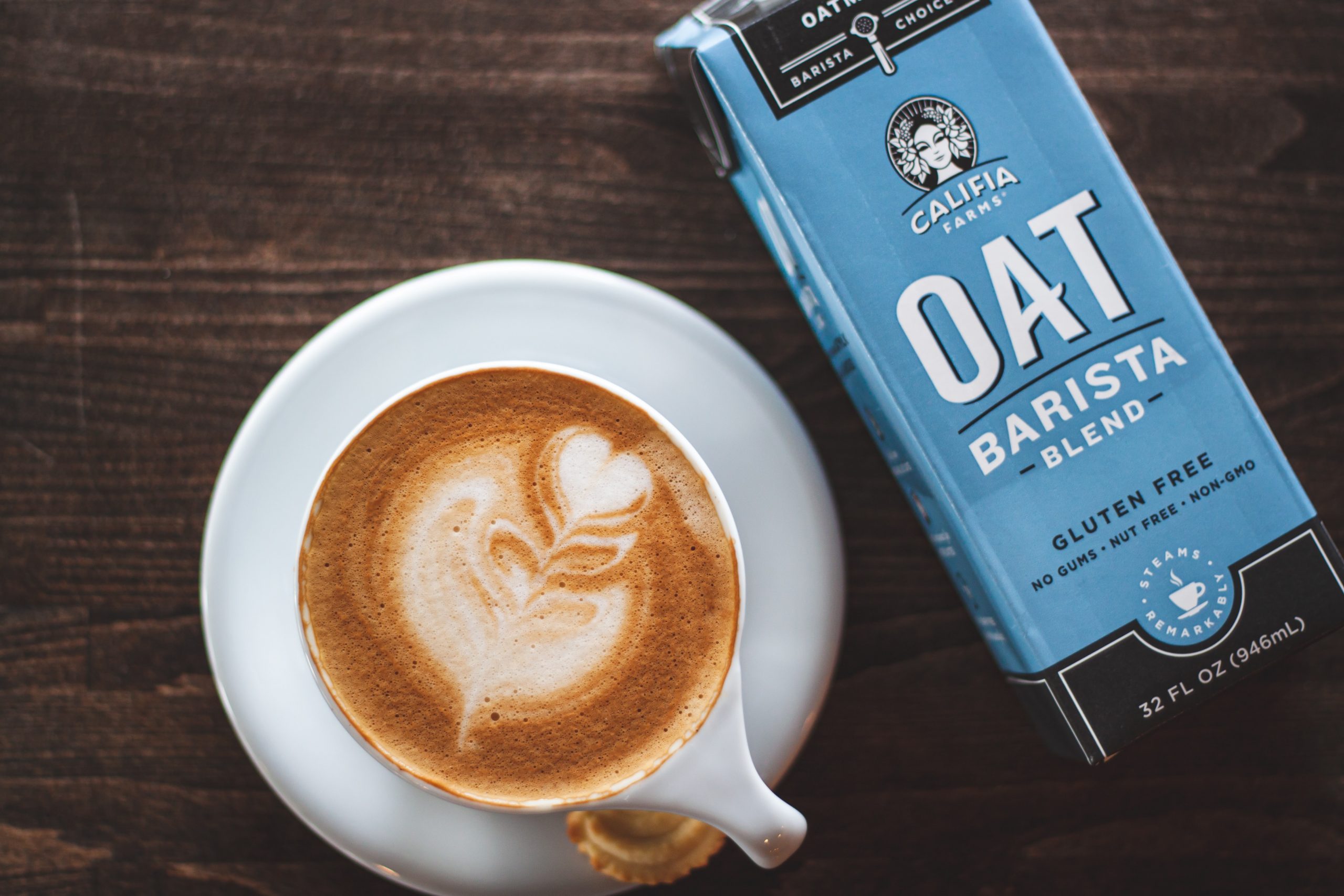 A cappuccino next to a carton of oat milk.