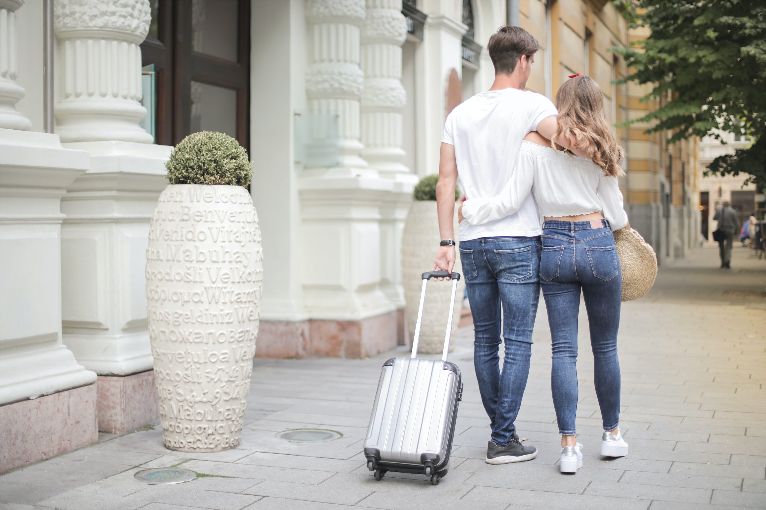 A young couple walk down the street with their luggage in tow.