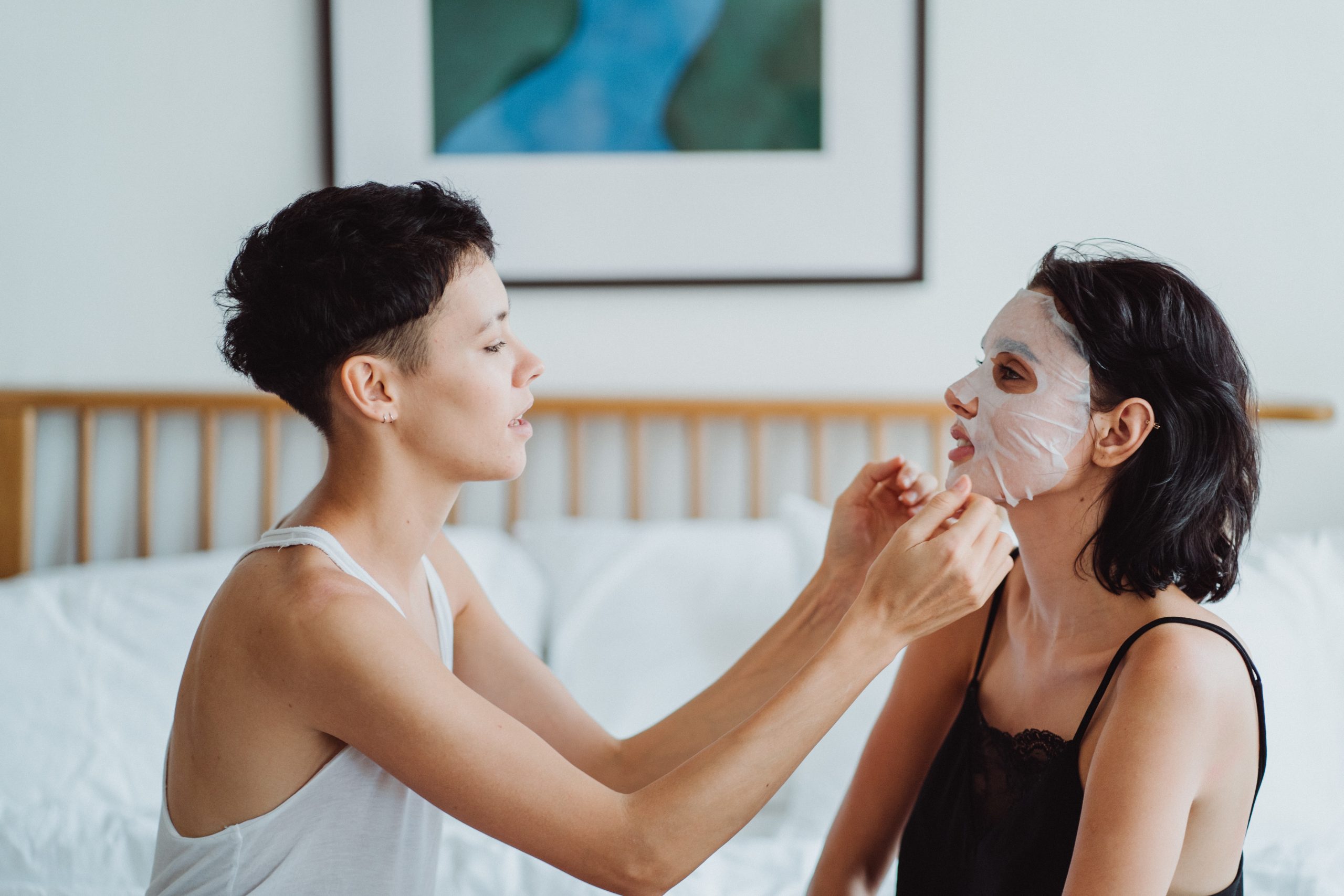 A young woman helps her friend apply a Garneir Sheet mask from the Garnier Sheet Masks Self-Care Collection.