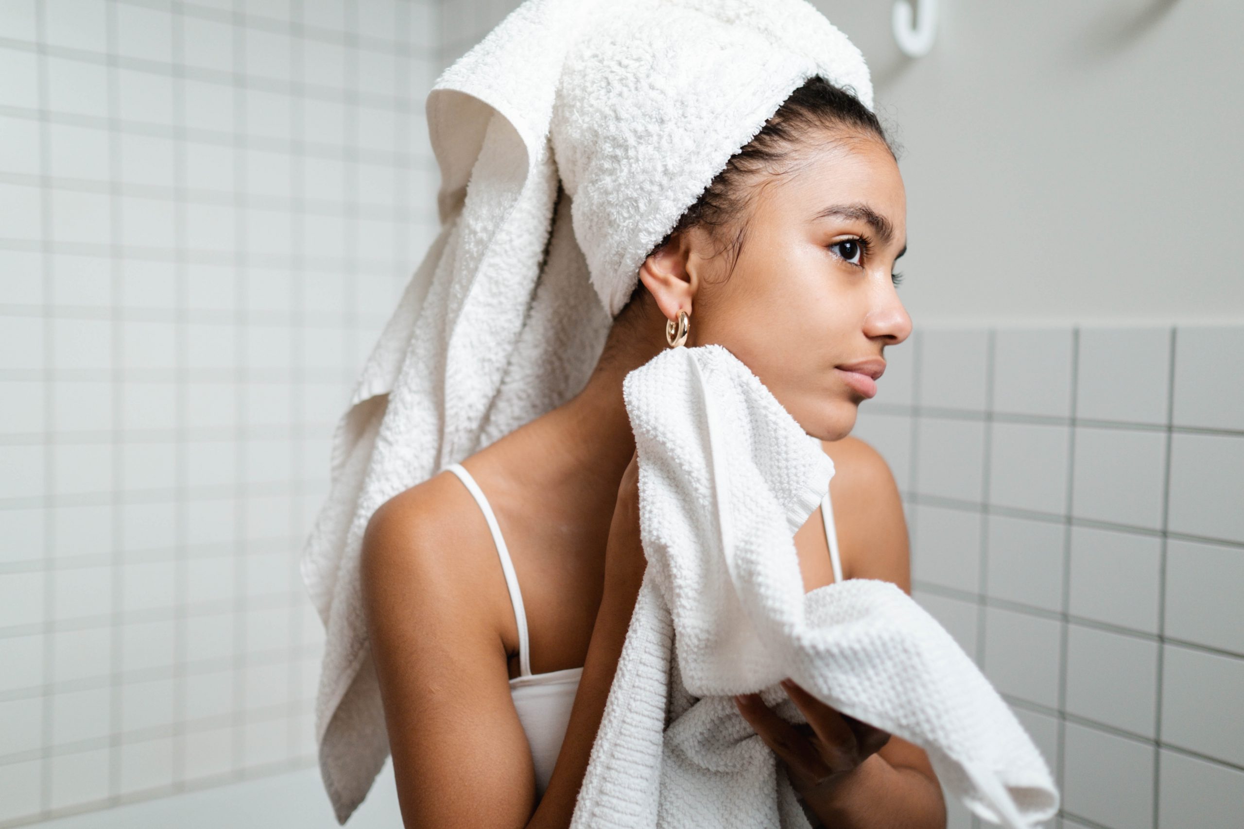 A young black woman in the bathroom mirror pampers her face with towel.