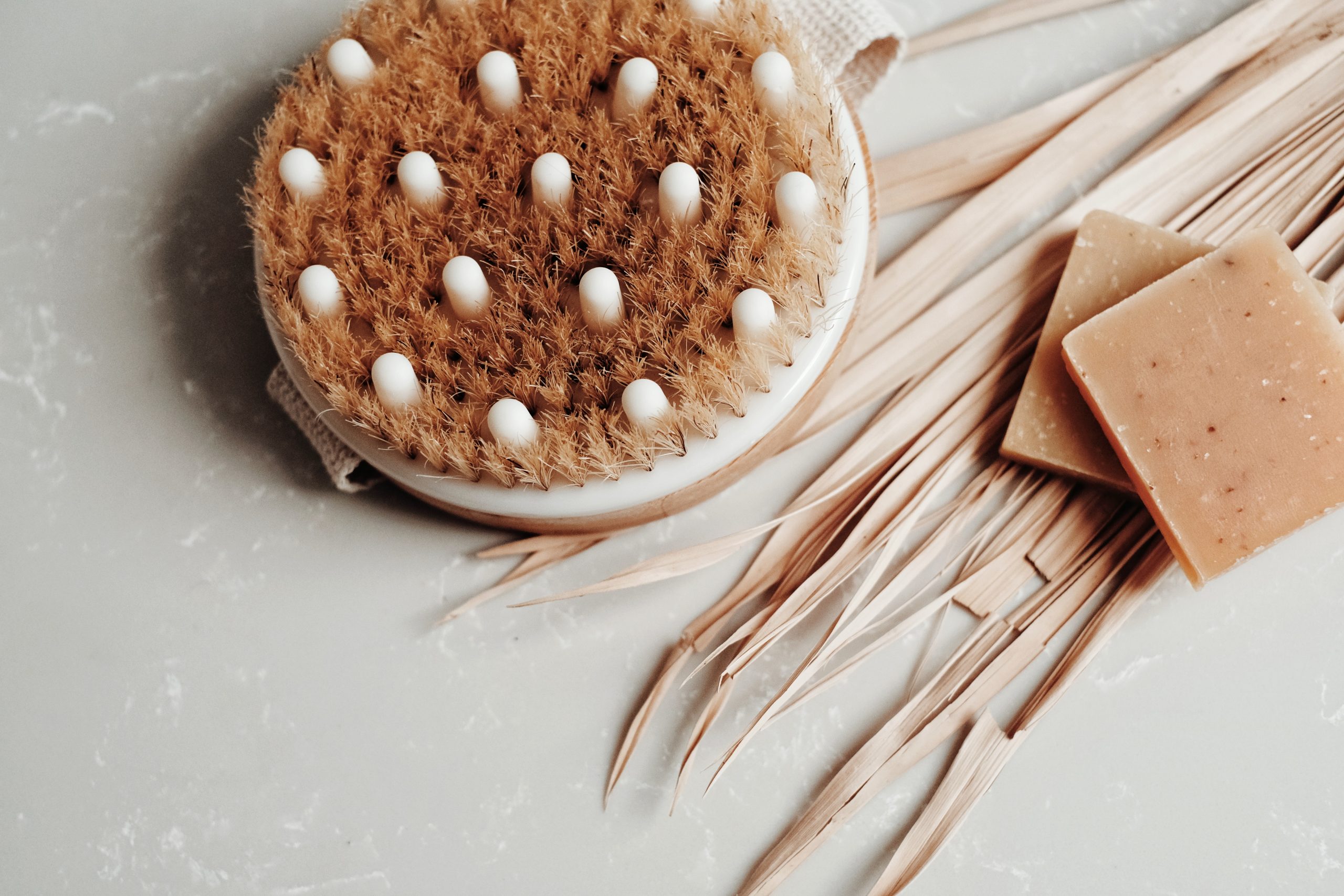 A brown scalp massager next to two brown soaps resting on a white tile.