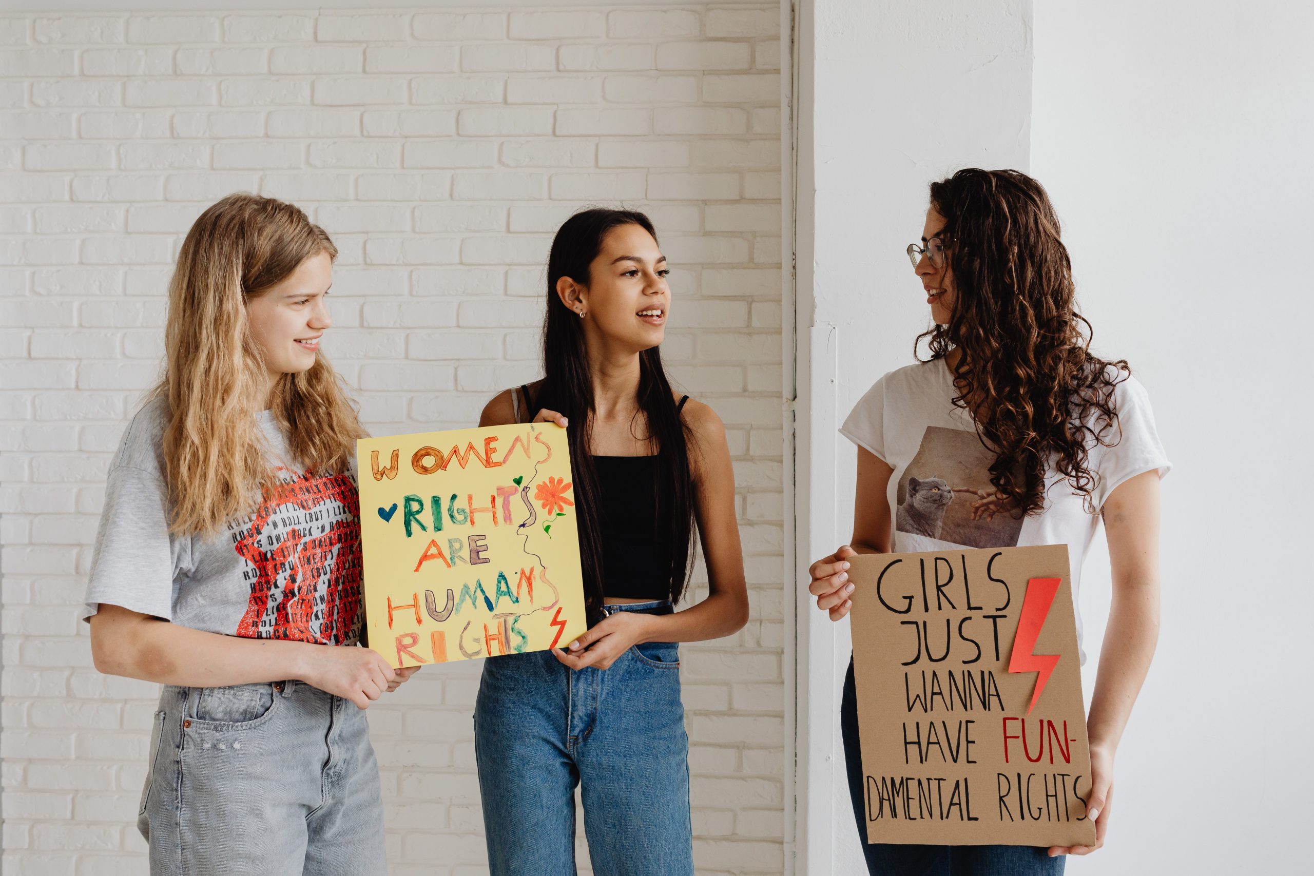 Three young women hold up signs protesting equal rights for women. 