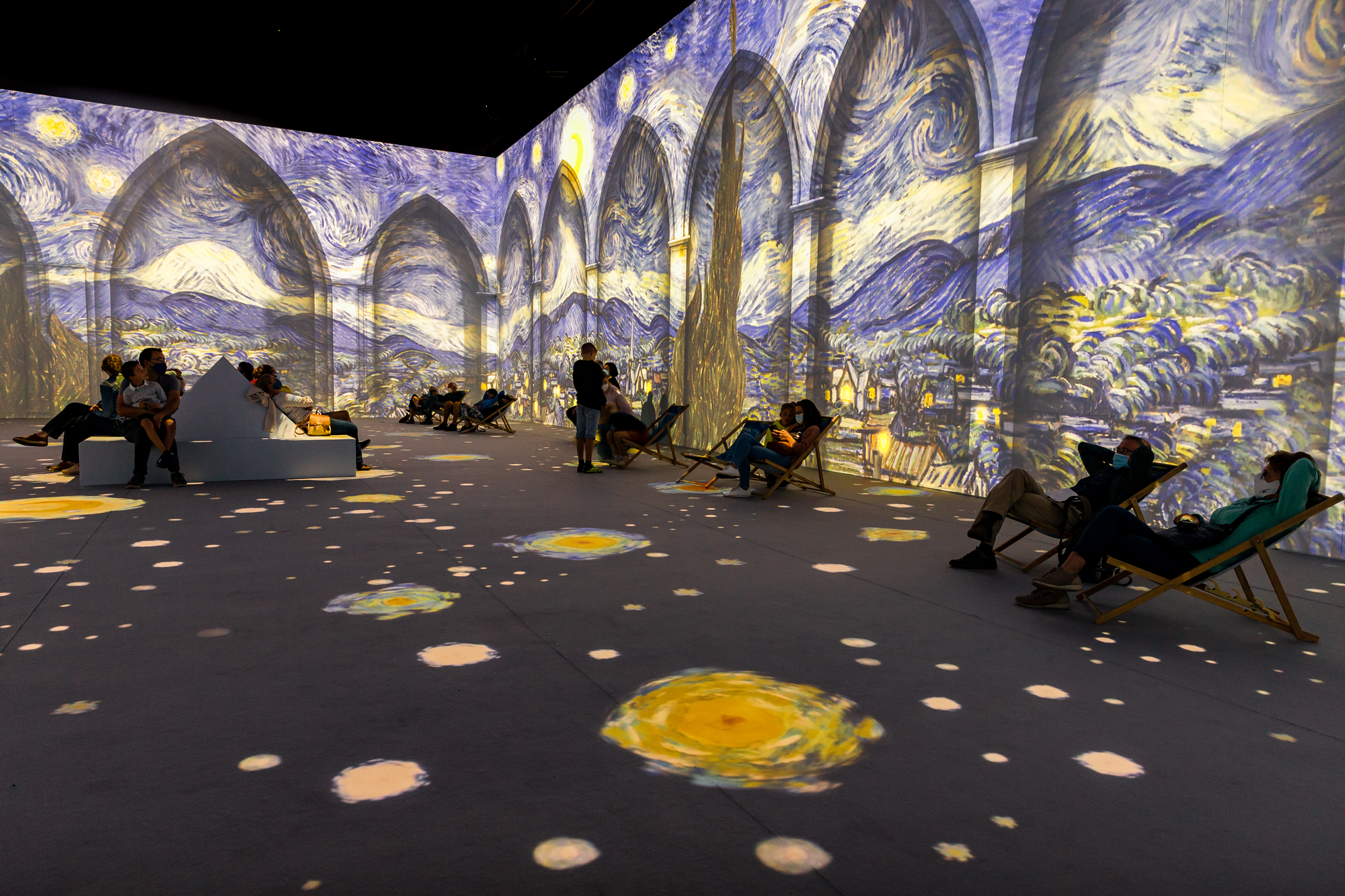 While relaxing on deckchairs and benches, people enjoy the animated show of Van Gogh: The Immersive Experience