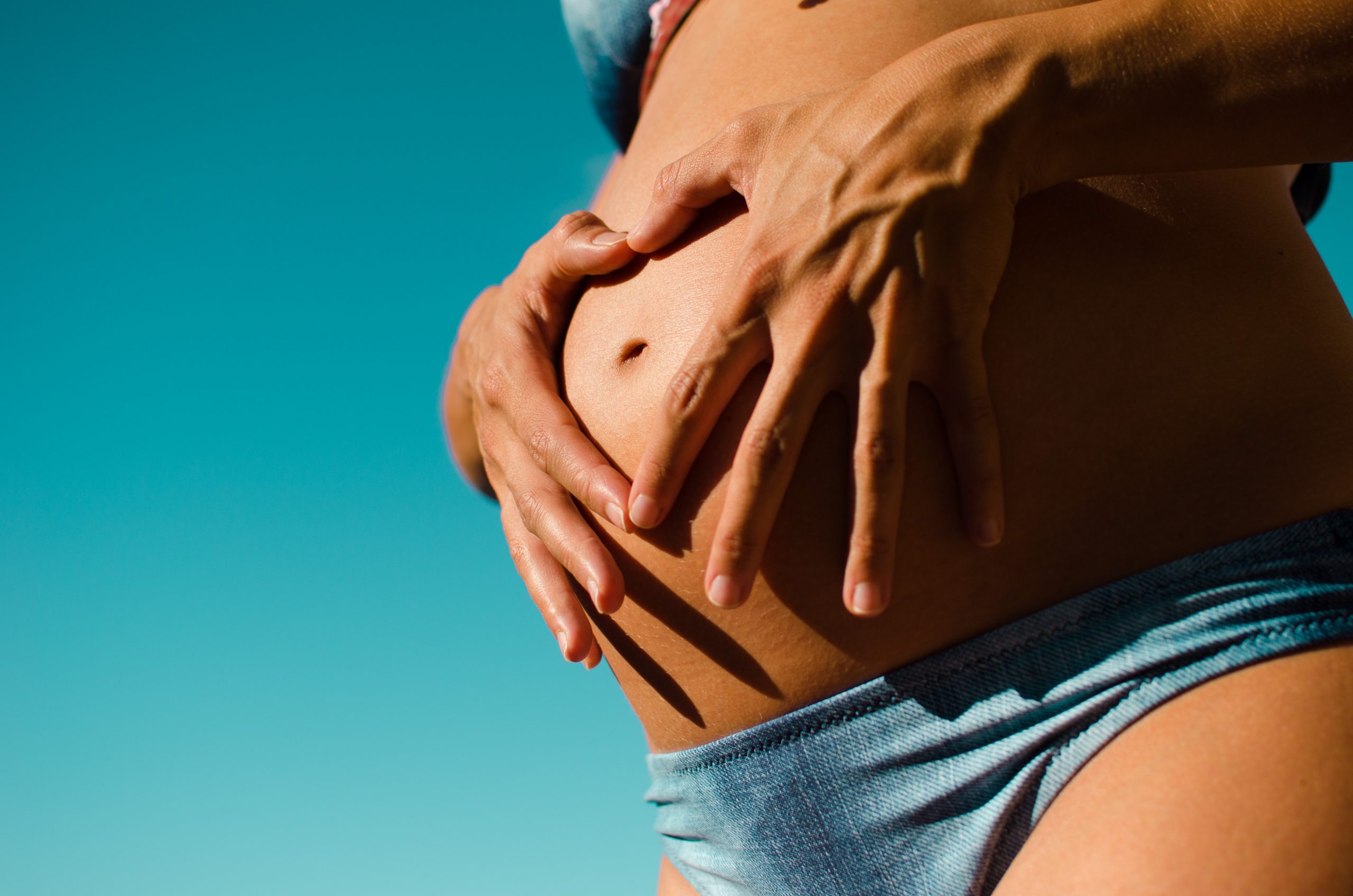 A young woman in a blue bikini holds her baby bump.