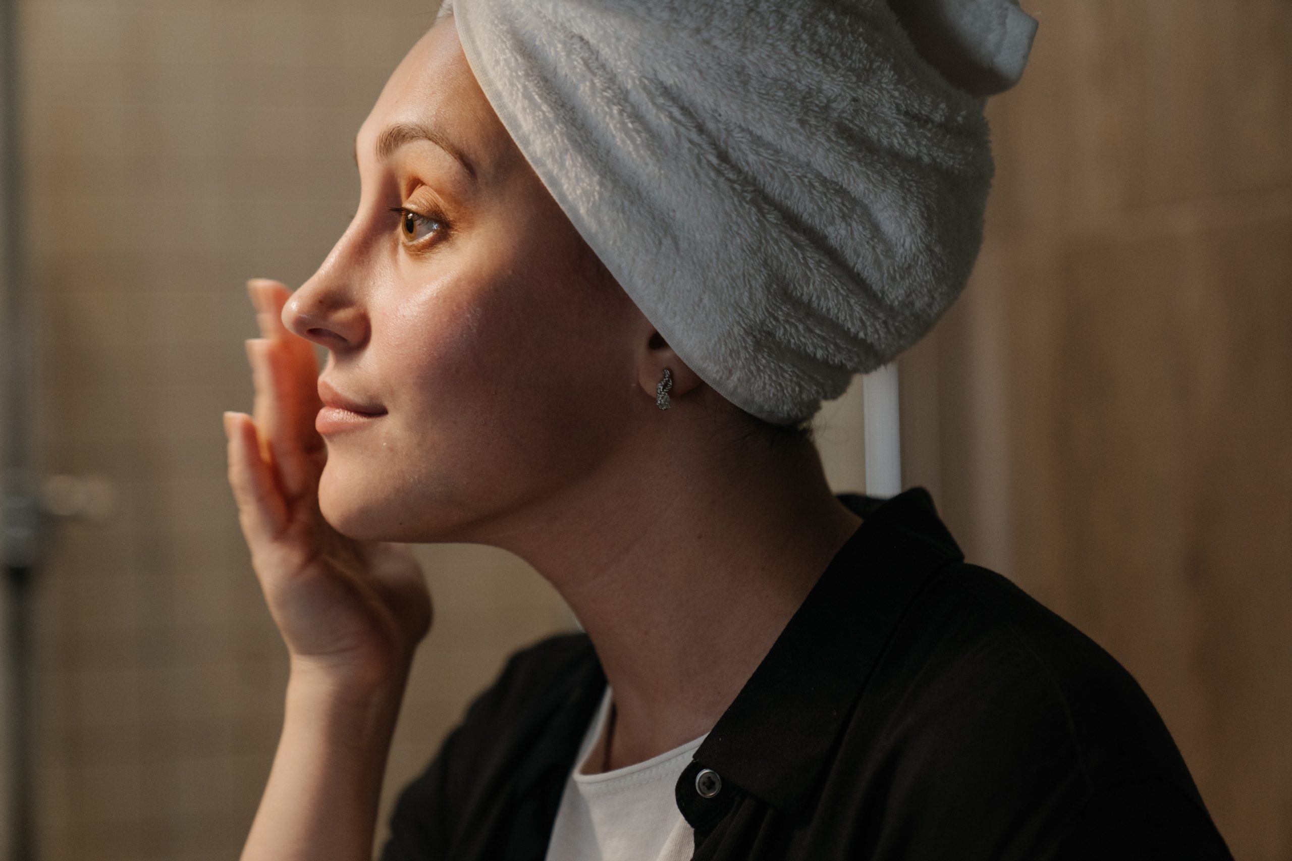 A side profile of a young woman moisturising her face in the mirror.