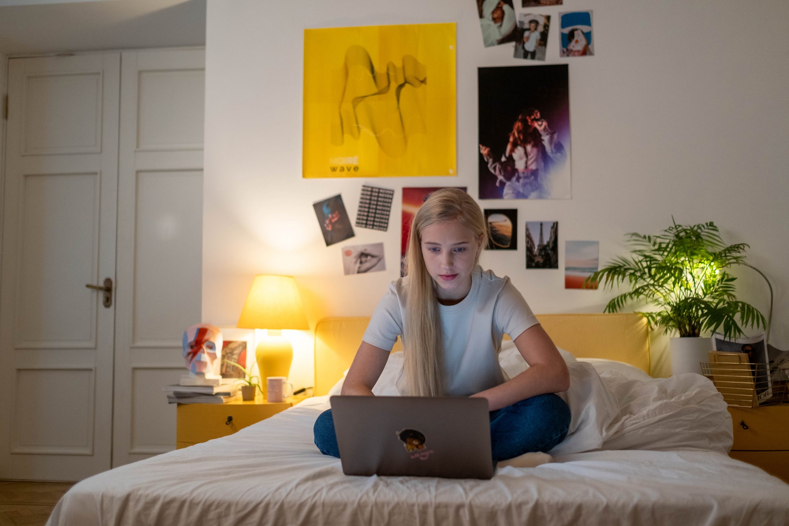 Sitting alone on her bed, a blonde teenager works anxiously on her MacBook.