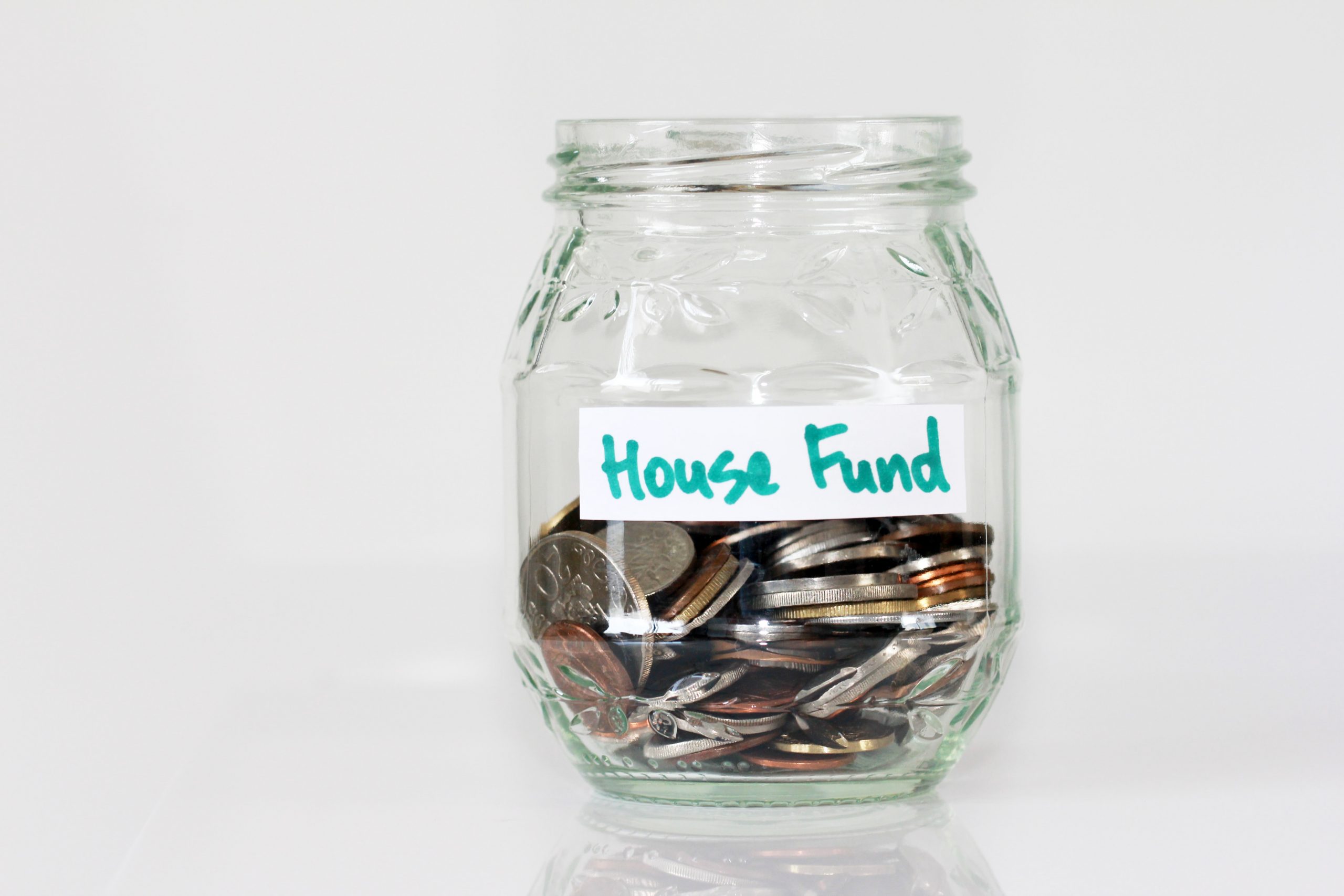 A glass jar of loose change with a hand-written label 'House Fund'.