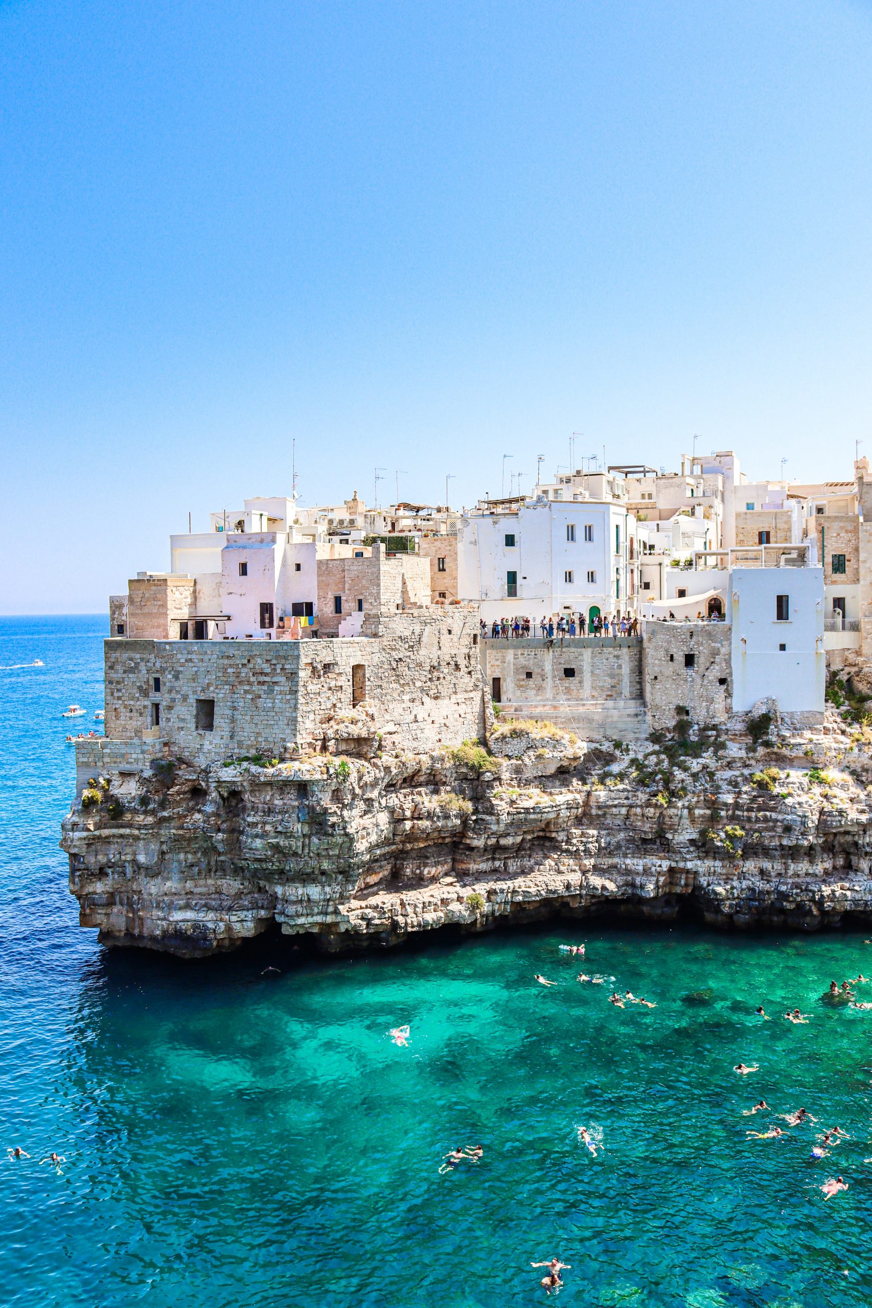 Swimmers enjoying a swim in the bay overlooked by the clifftop houses of Bari, Italy.