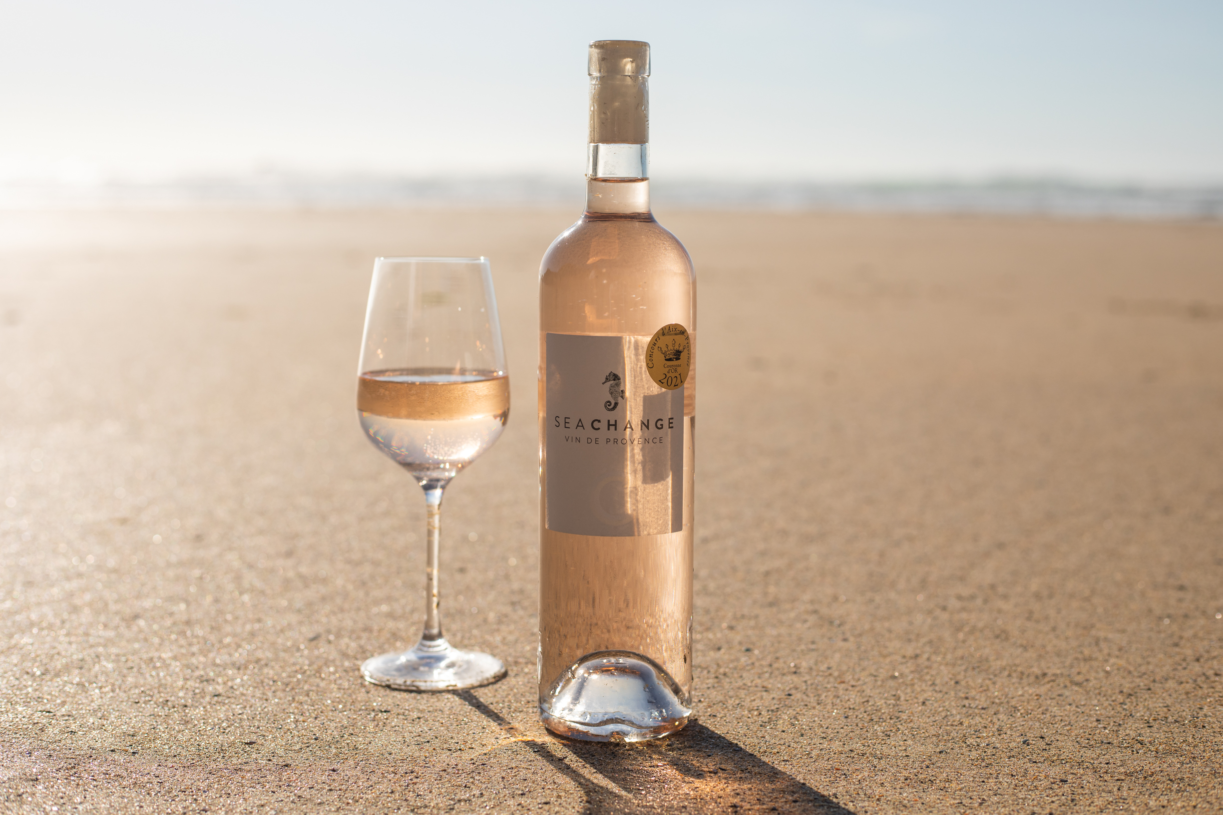 Out in the desert sand, a bottle of Sea Change rosé with a glass next to it.