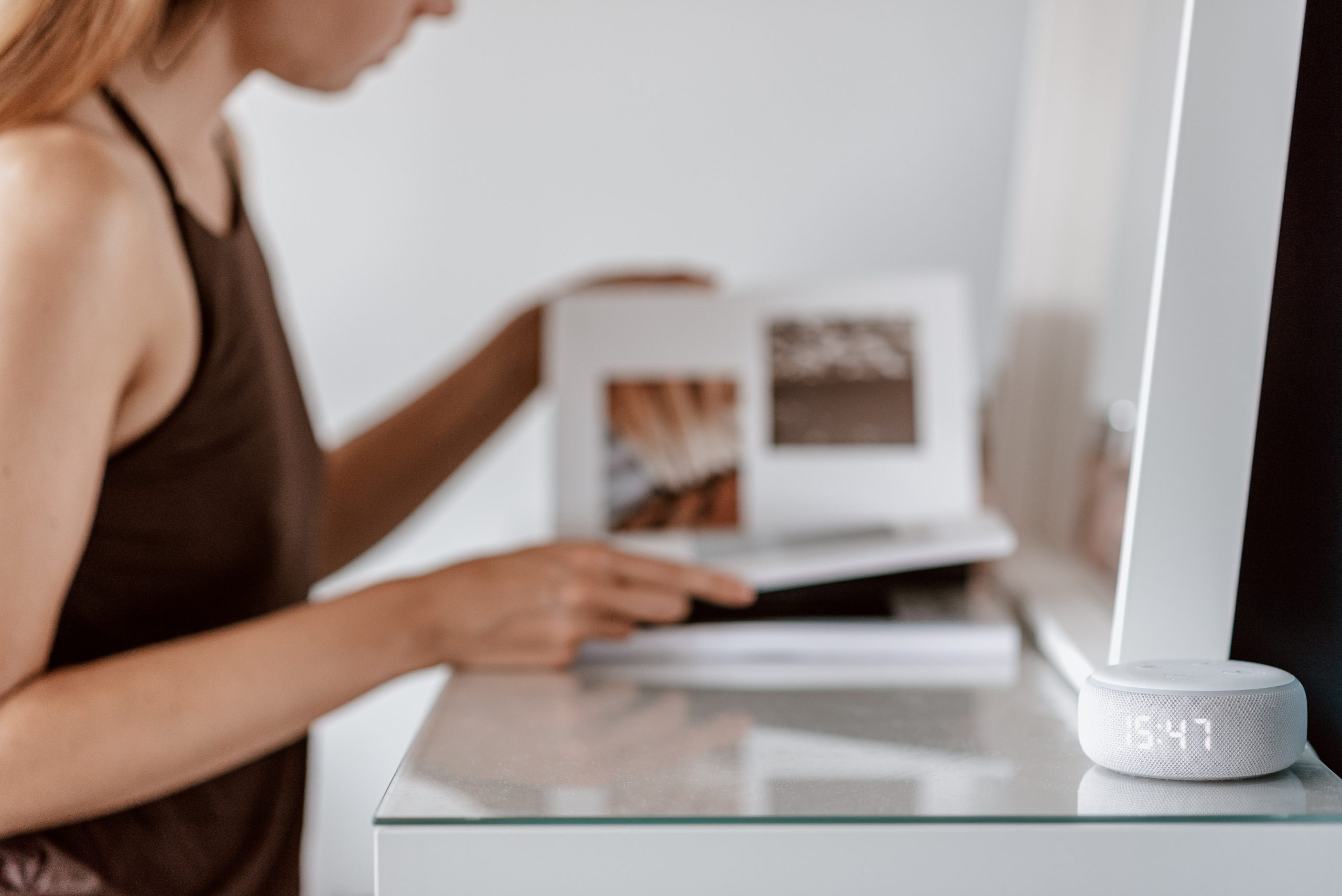 A smart device operating in the foreground as a woman reads a magazine at her desk.