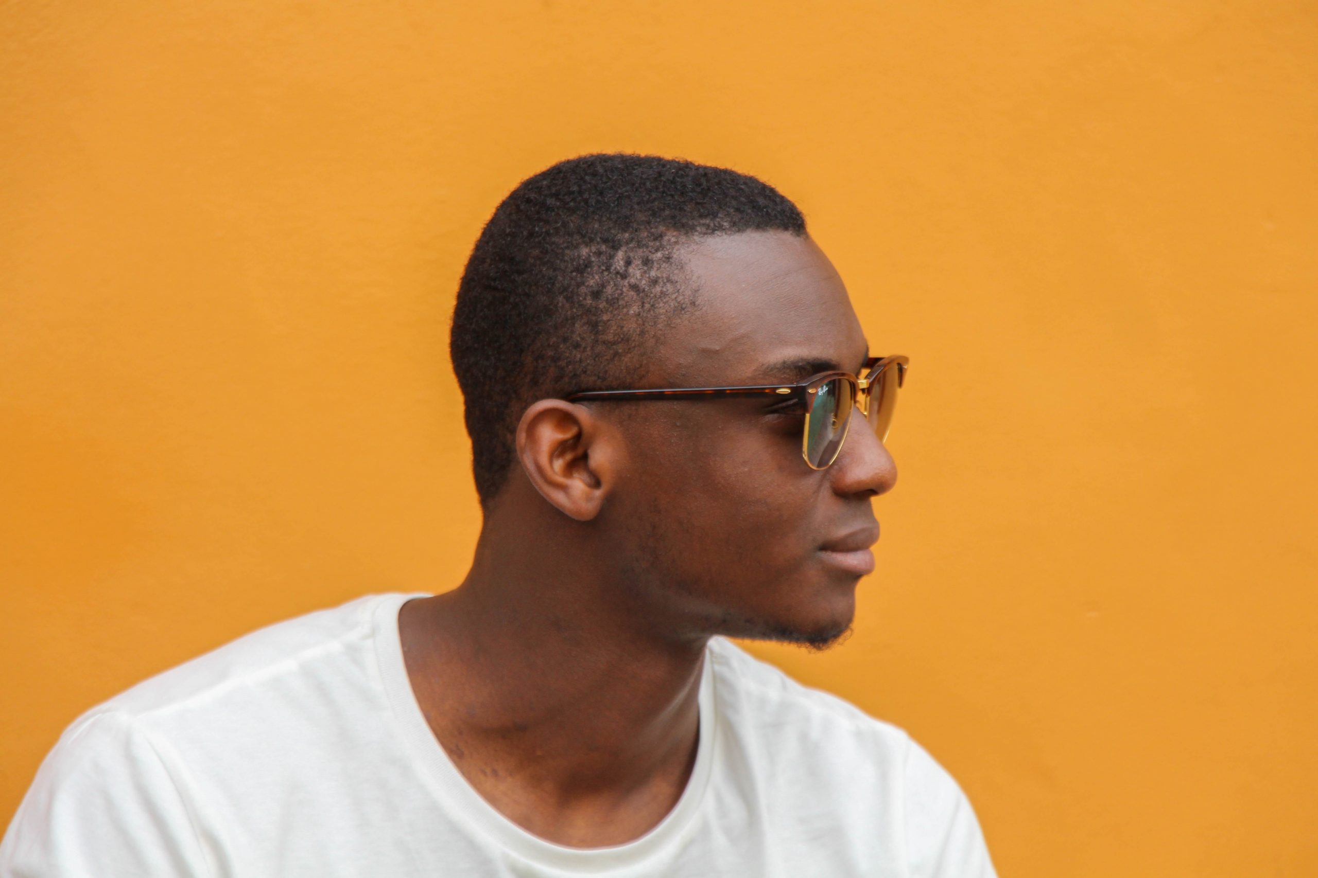 A young man modelling Ray-Ban Rb3016 Clubmaster Square Sunglasses against an orange backdrop.