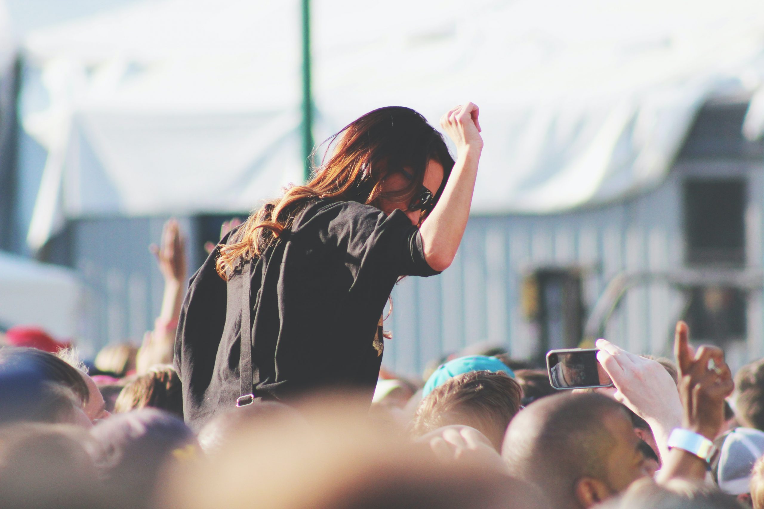 At a music concert, a woman with sunglasses sits on her friend's shoulder piggyback to see better.