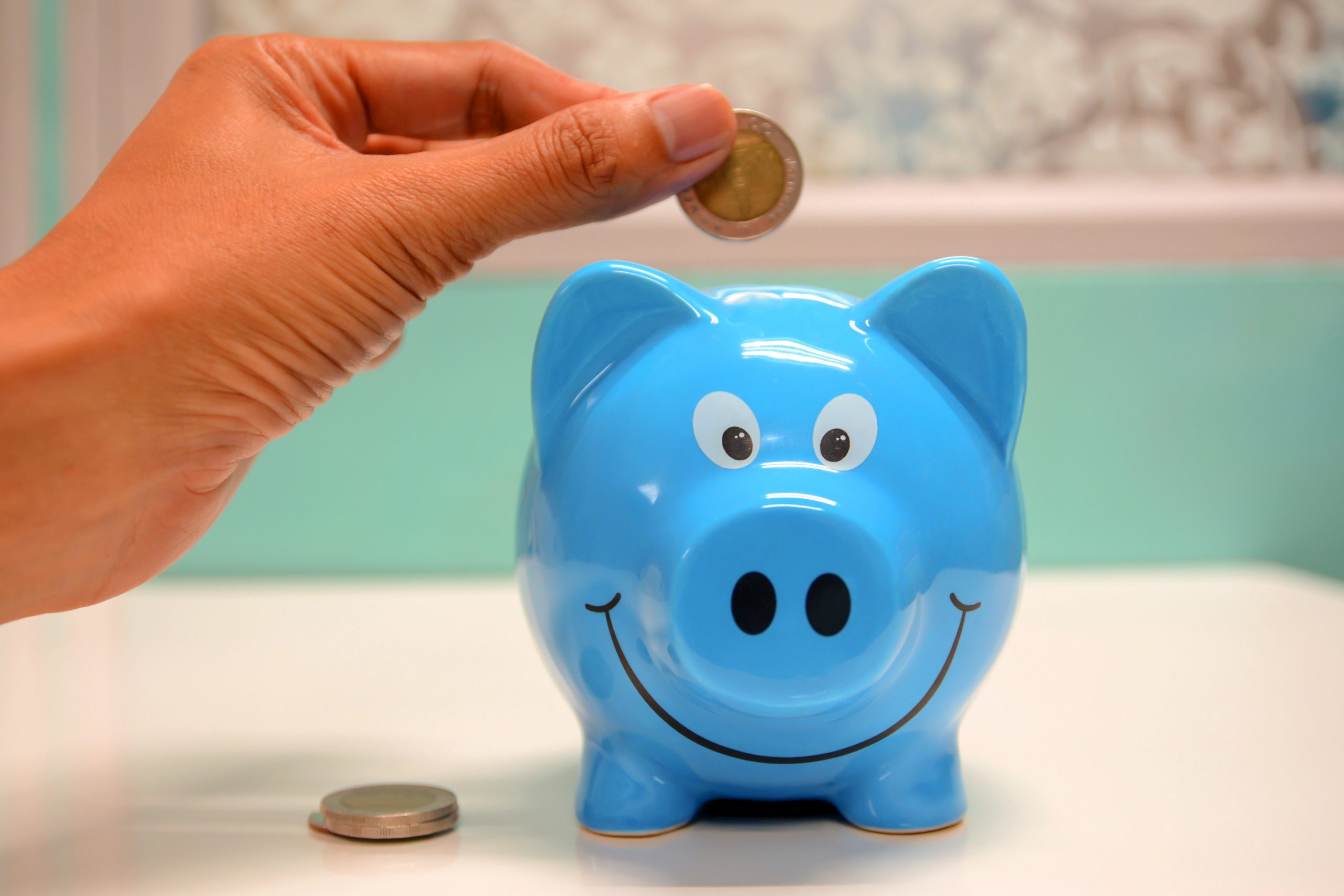 A hand putting coins into a blue piggybank.