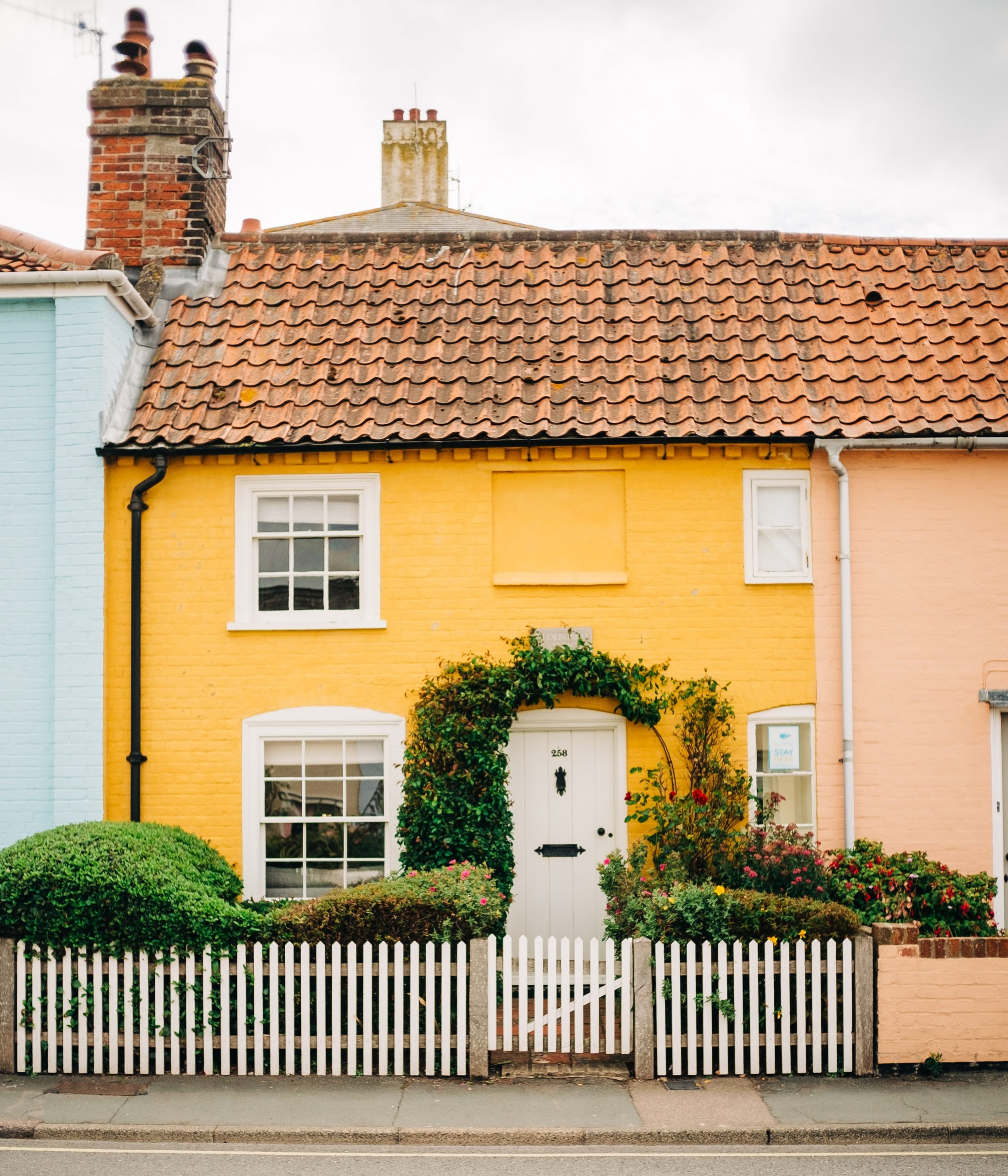 Behind a white picket fence, a terraced English home painted sun yellow, with an inviting front garden.