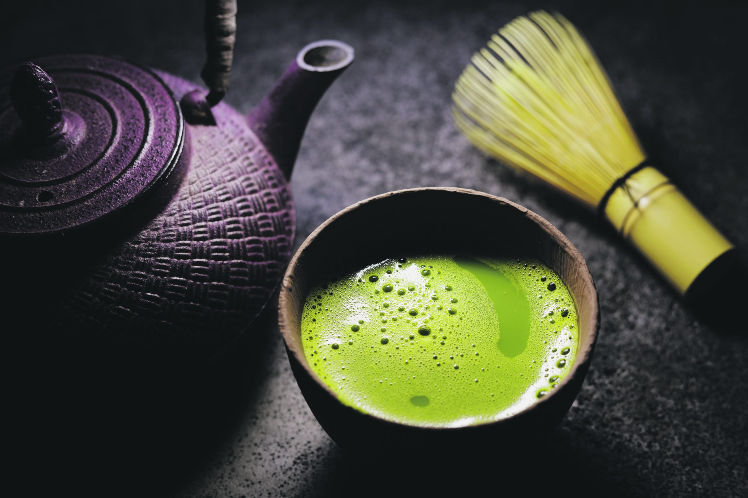 A cup of green matcha tea next to a cast iron kettle.