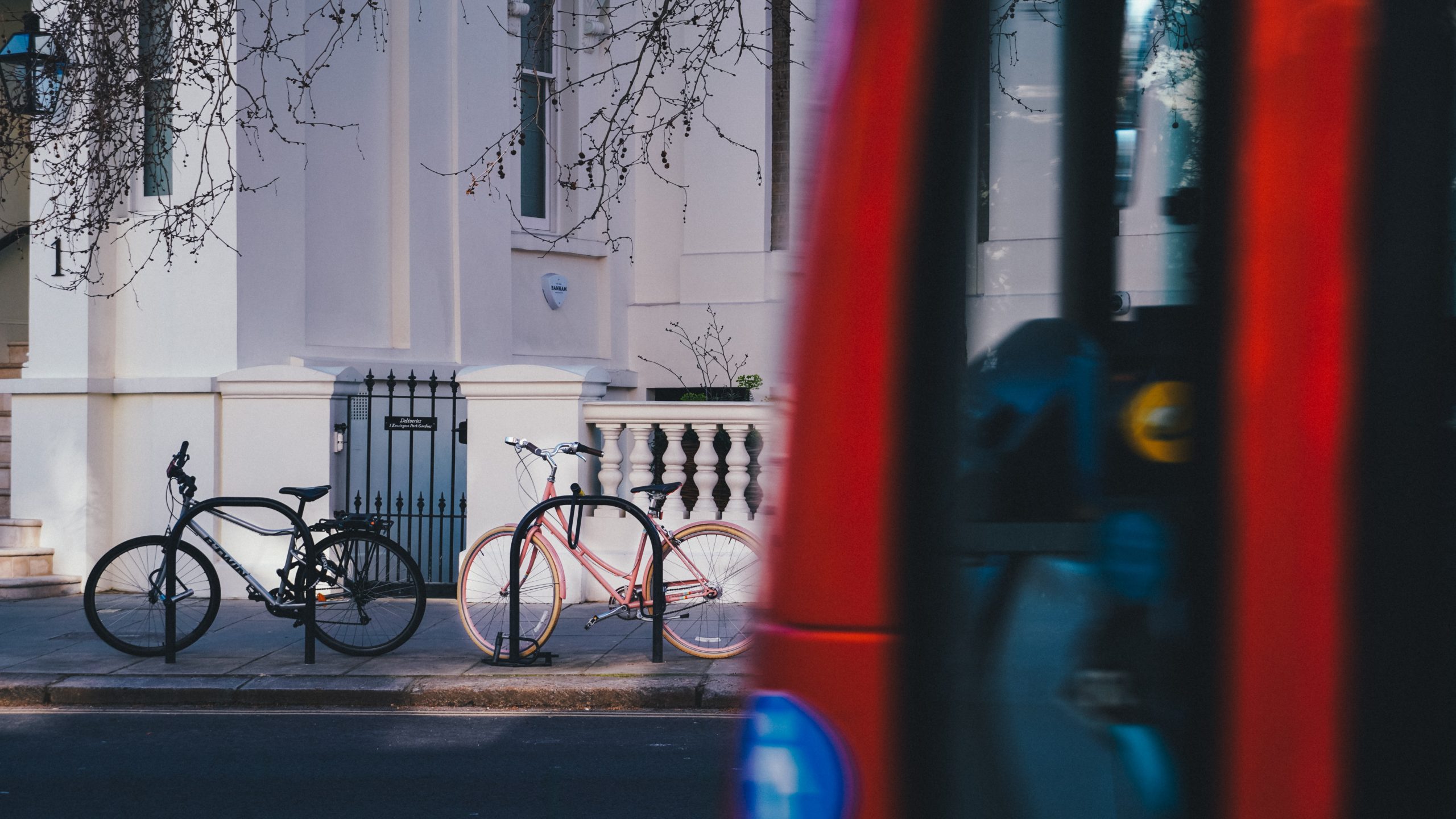 One black bicycle and one pink bicycle parked on cycle stands on a street in London.