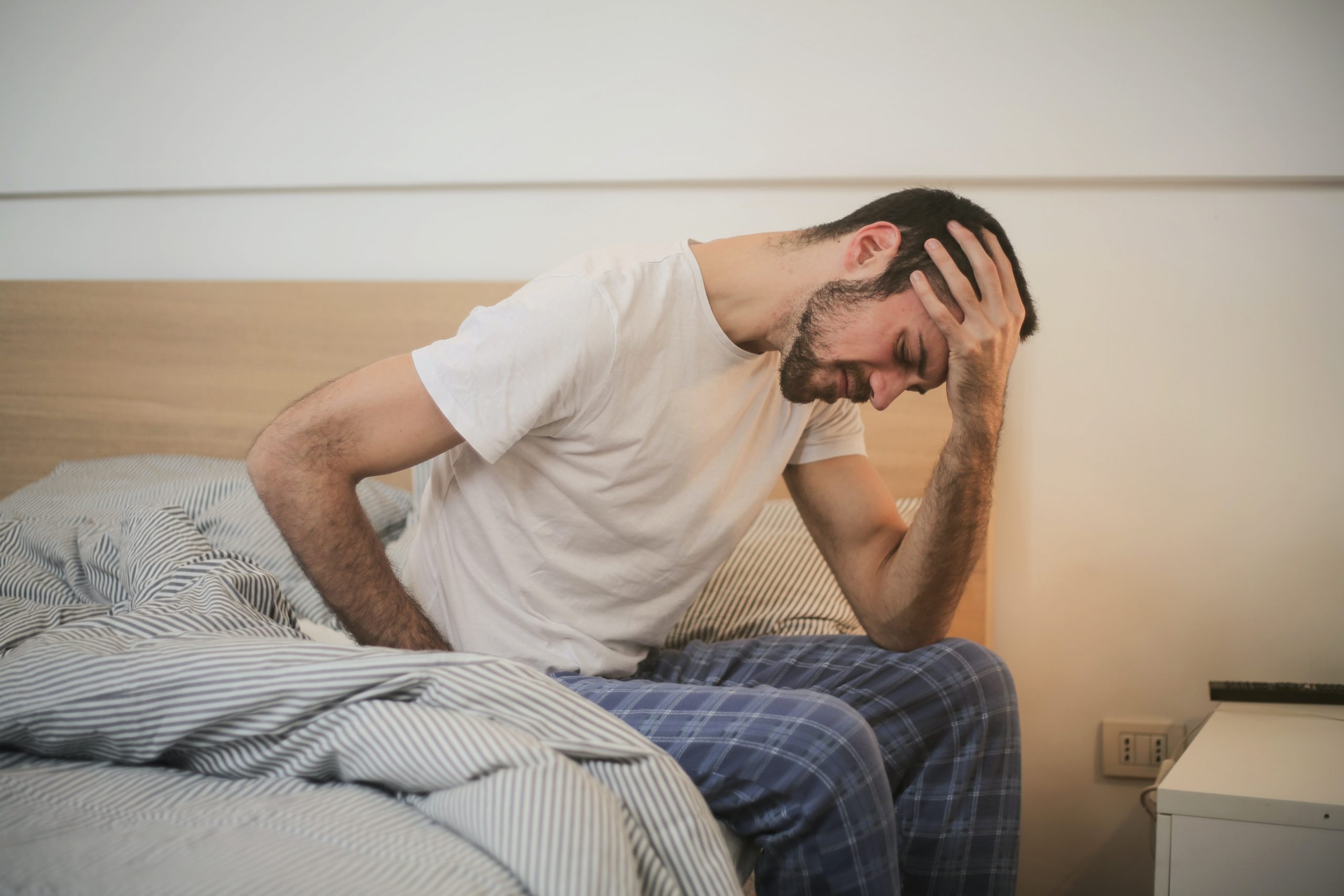 A man cramping in pain while sitting on the edge of his bed after waking.