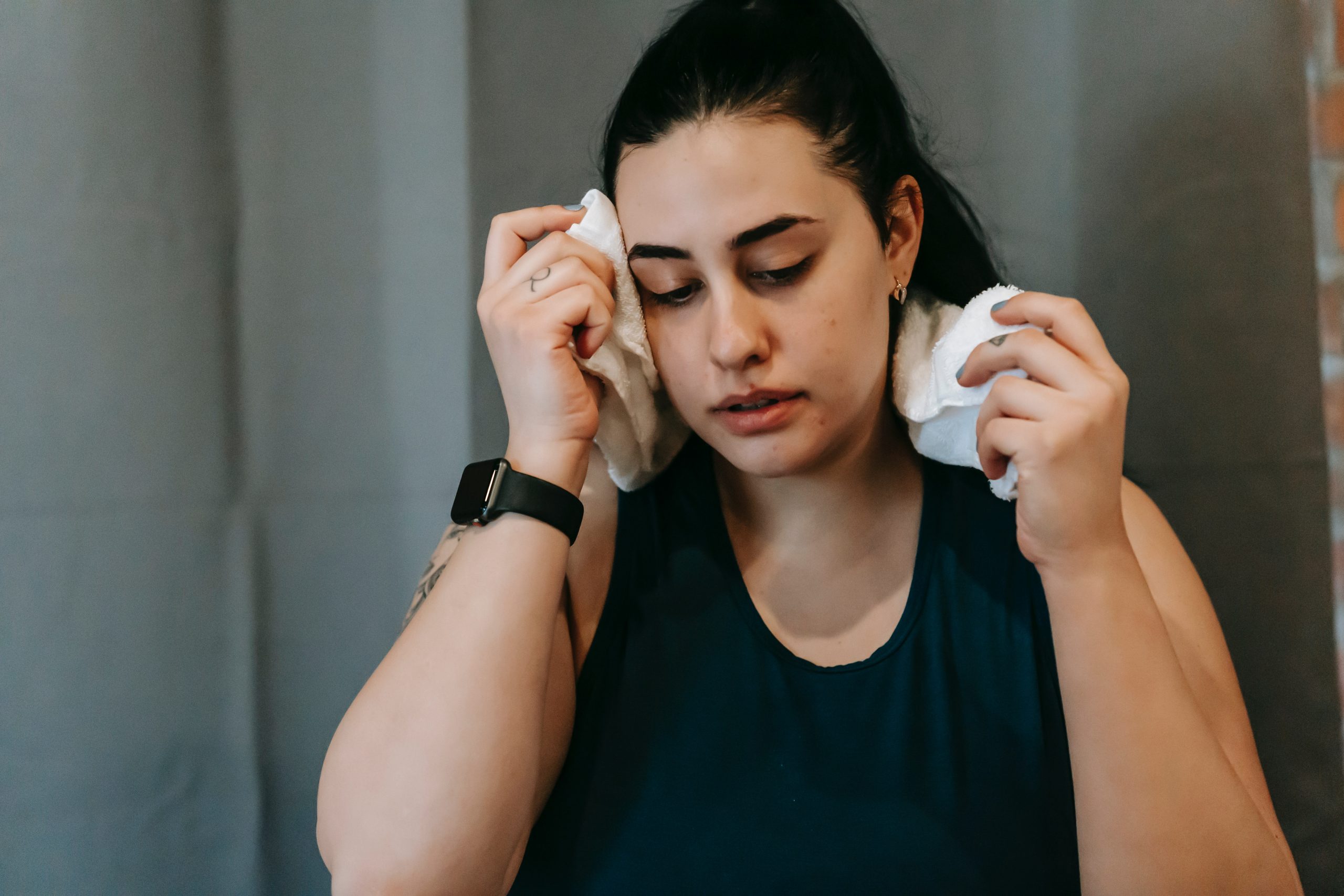 A young woman dabbing a hand towel to her face to keep cool in the warm weather.