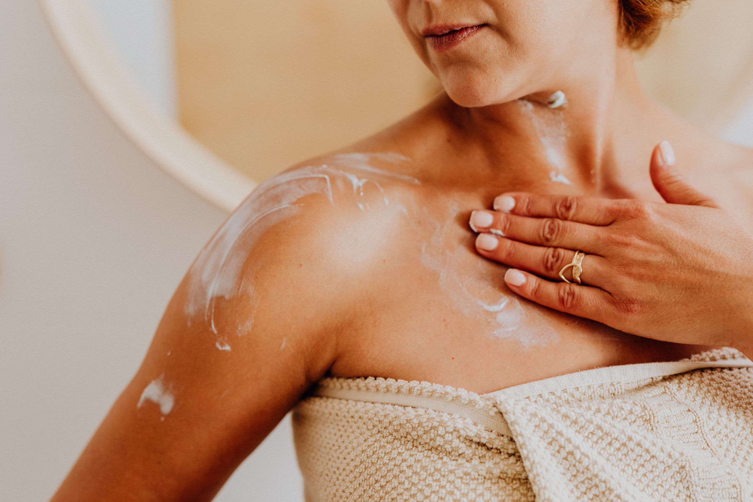 A woman applying sunscreen to her bare shoulders and torso after a bath.