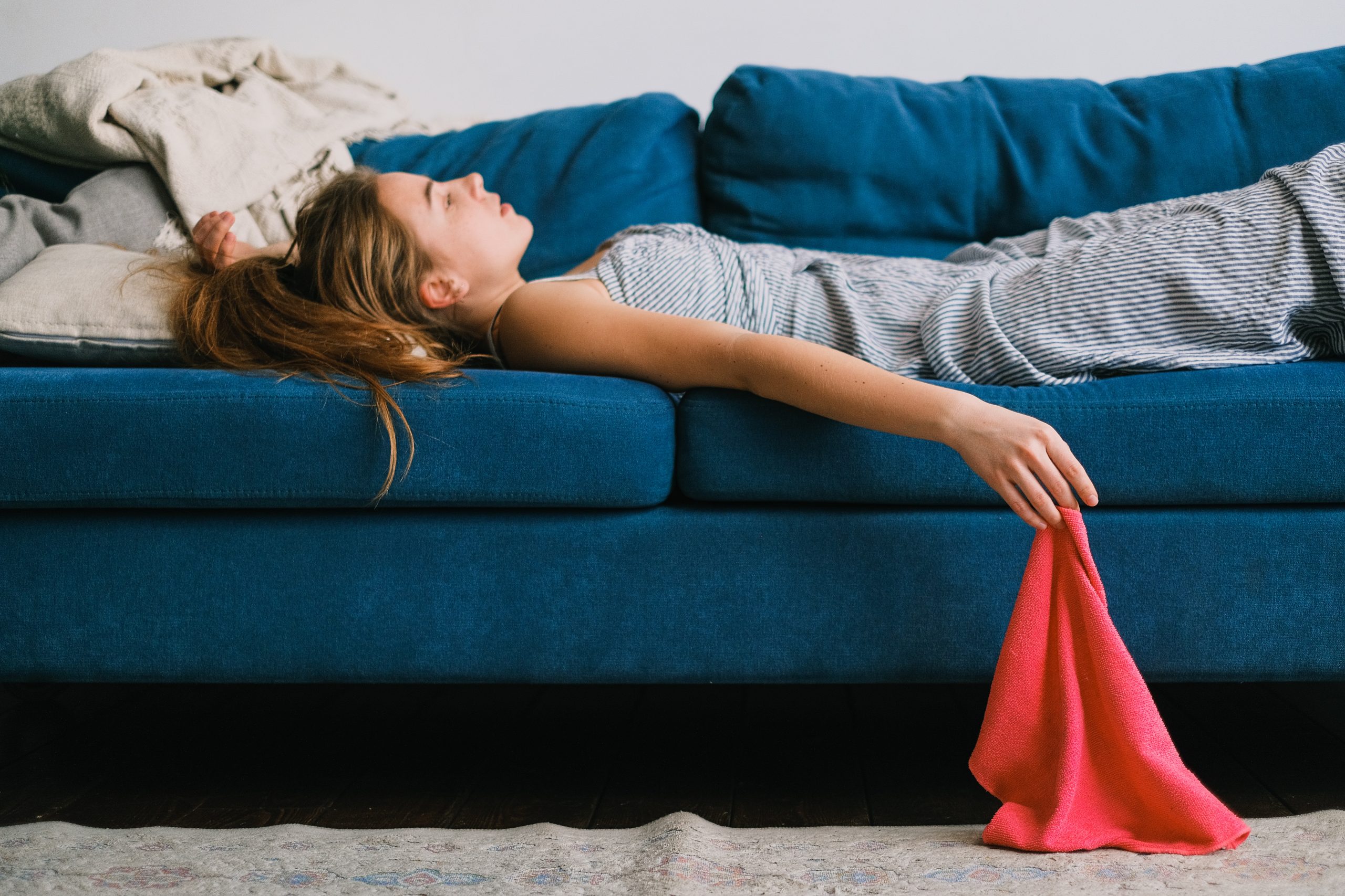 Lying down on a blue sofa, a young woman tries to keep cool with a red hand towel.