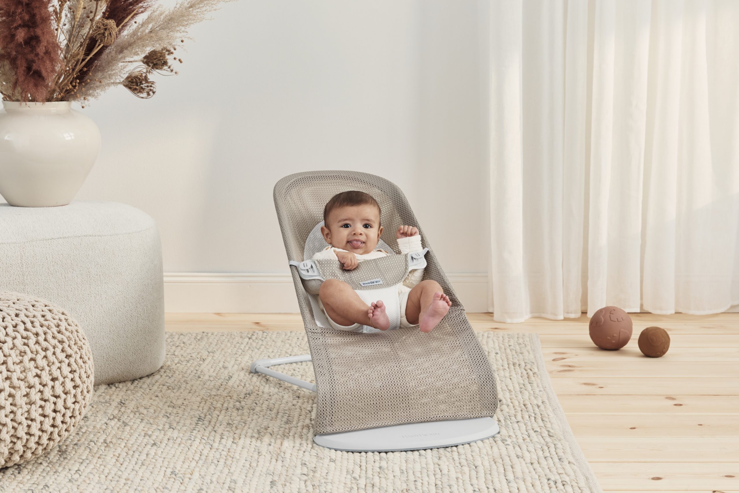 A happy baby gently rocking in a BabyBjörn Bouncer seat.