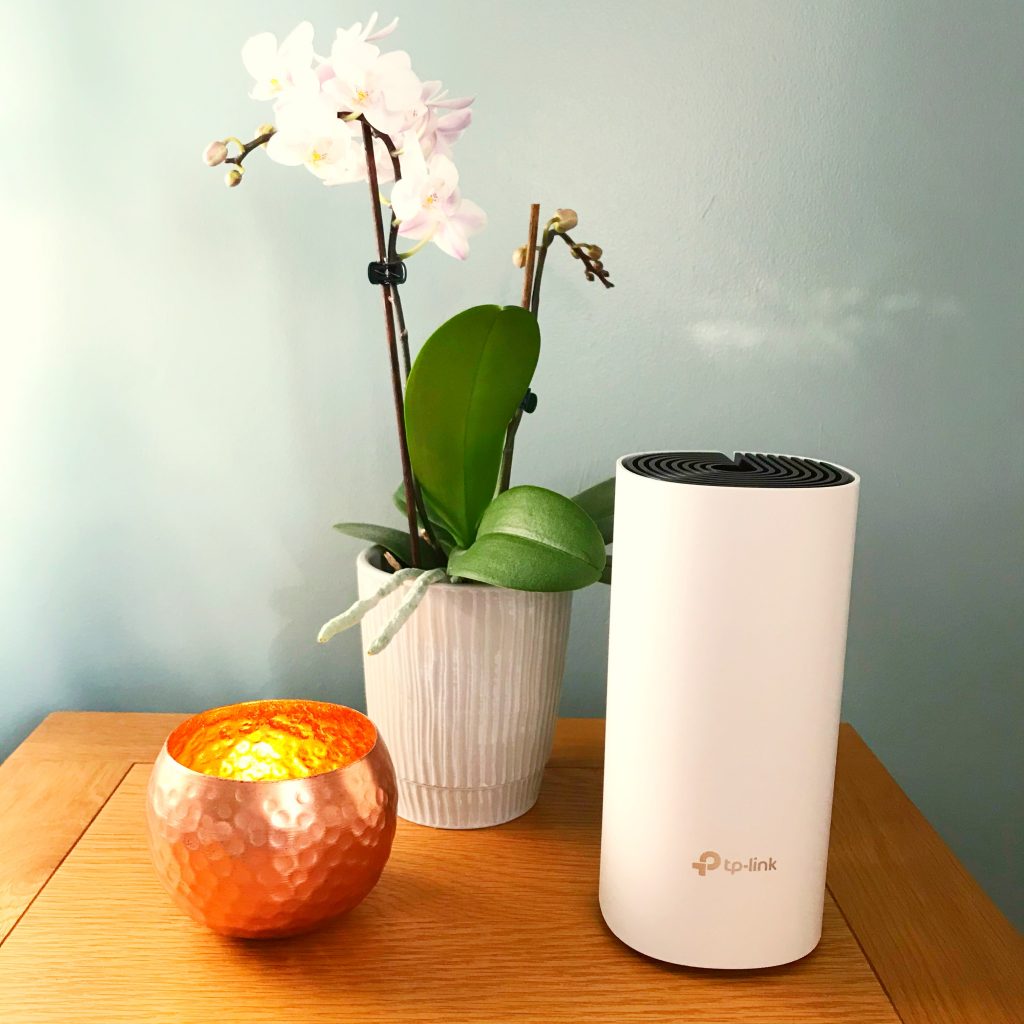 On a corner table: a light, an orchid and the three-unit TP-Link Deco M4.