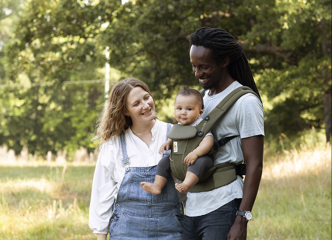 A mixed race couple taking a walk in the park, carrying their baby in a Ergobaby Omni Breeze baby carrier.