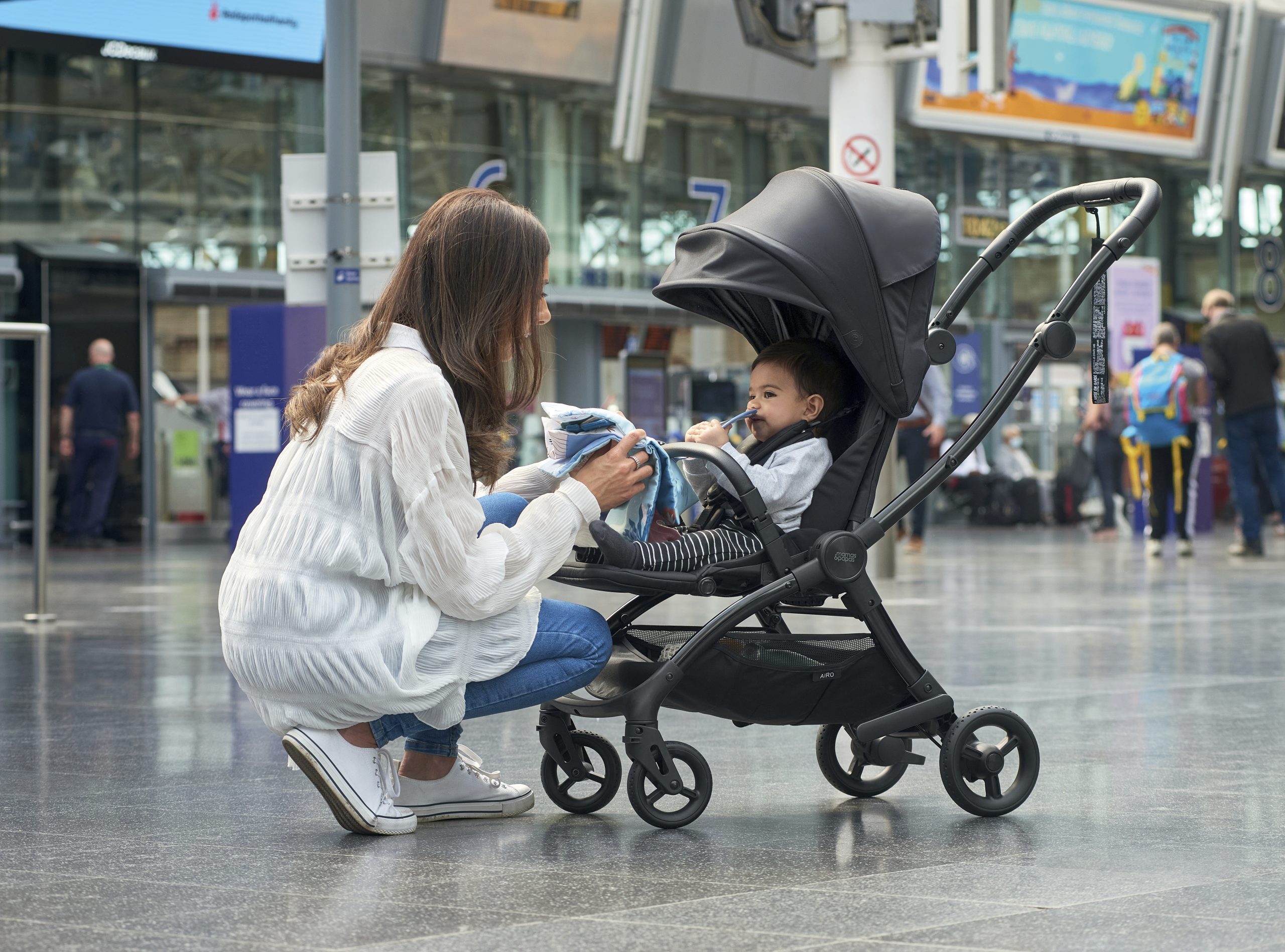 At a railway station, a young mother cares for her child sitting in a pram.