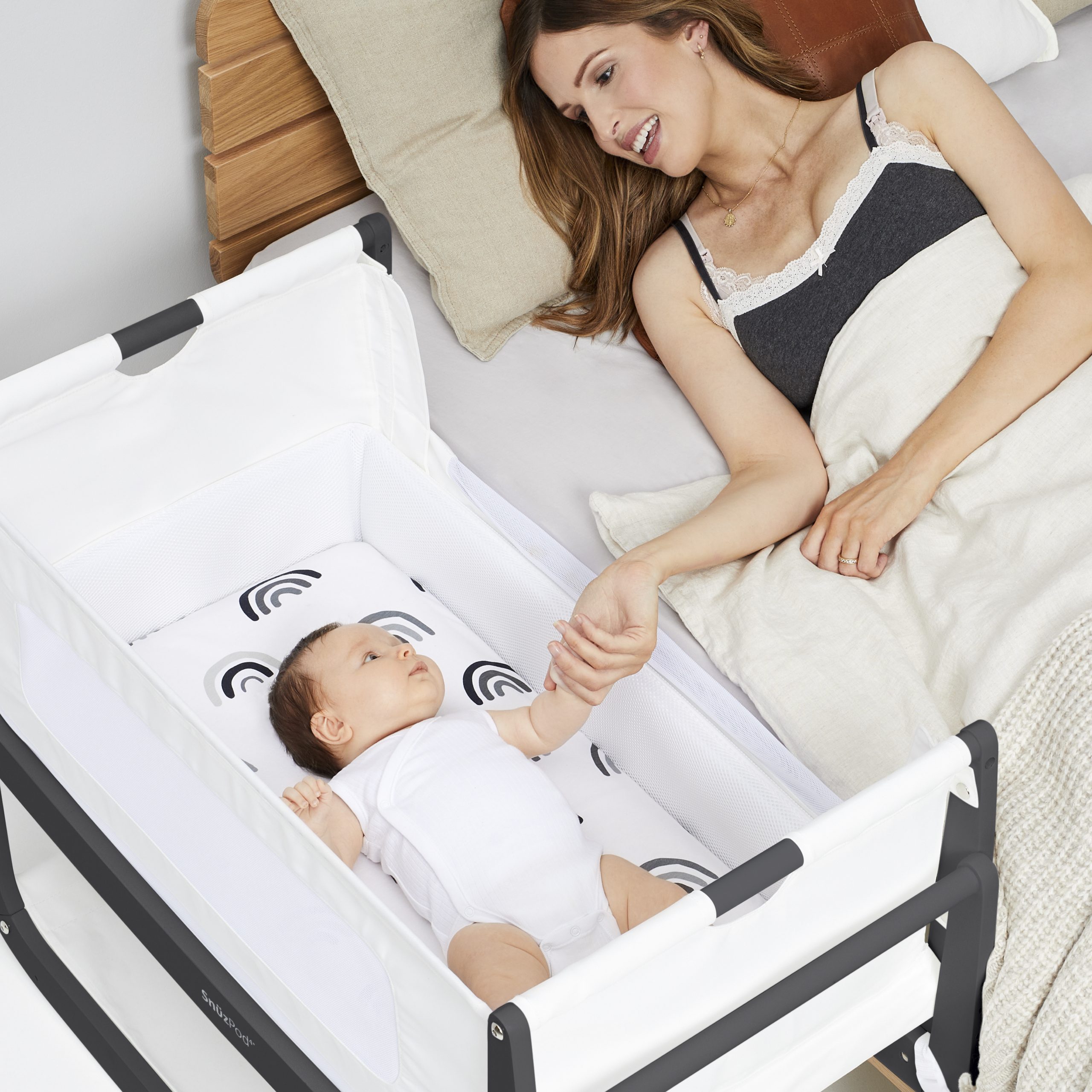 A young mother in her bed reaching over to comfort her baby lying in his cot.