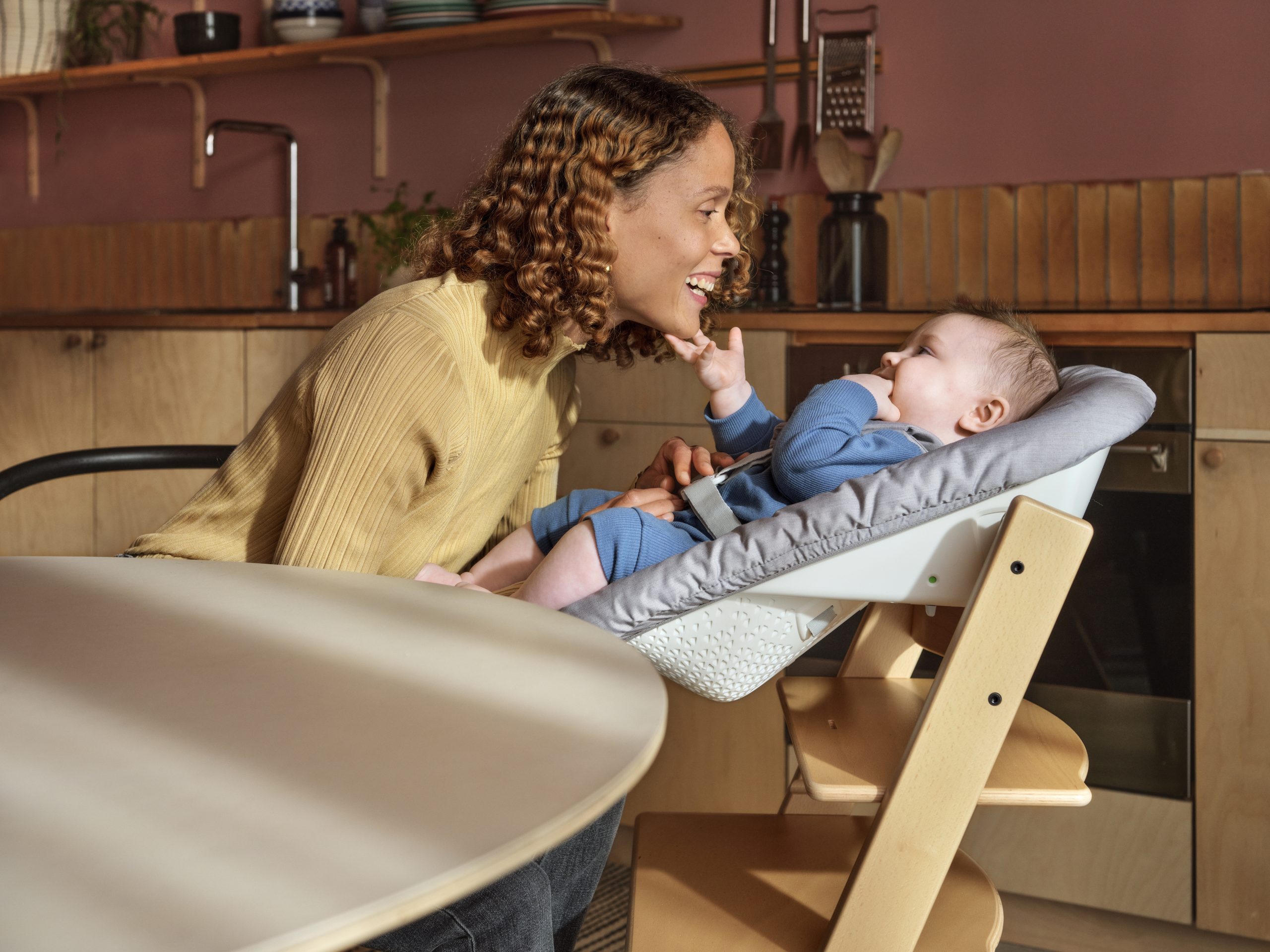 A baby in a Stokke Tripp Trapp Chair listening to his mother next to him.